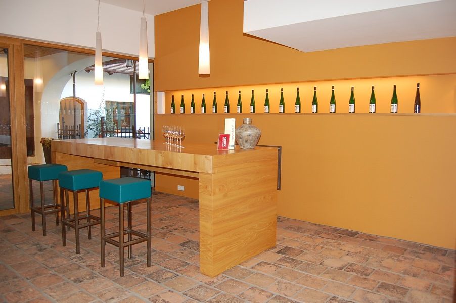 Moderner Verkostungsraum mit Holztresen, Barhockern und Weinflaschen an der Wand.