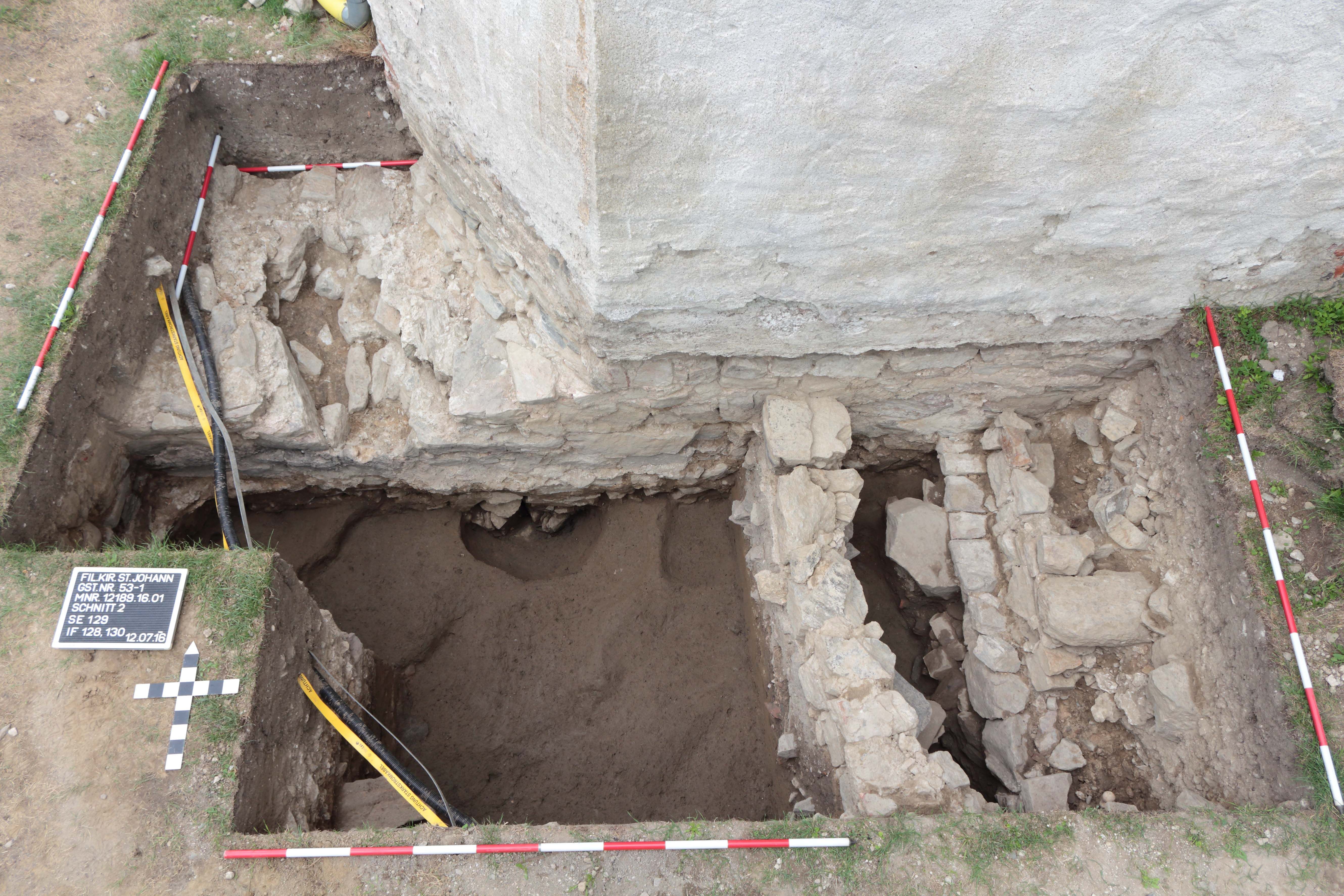 Archäologische Ausgrabung mit freigelegten Mauerresten und Messlatten.