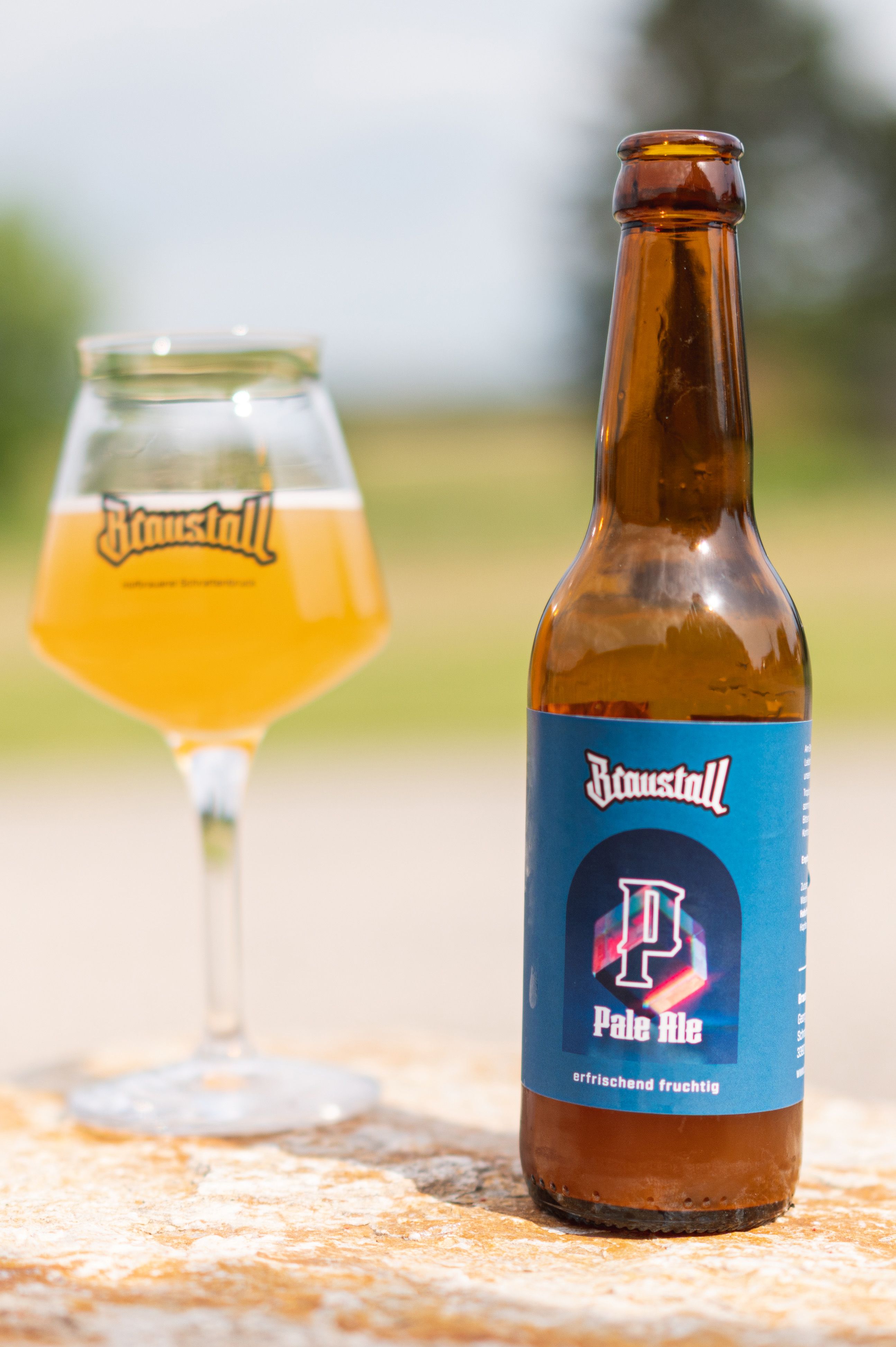 Eine Flasche Braustall Pale Ale und ein Glas mit Bier auf einem Tisch im Freien.