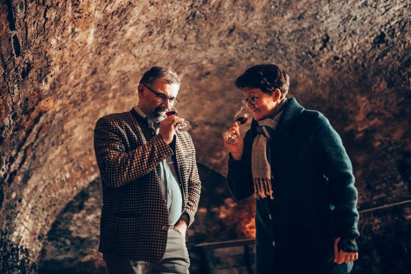 Two people taste wine in a wine cellar.