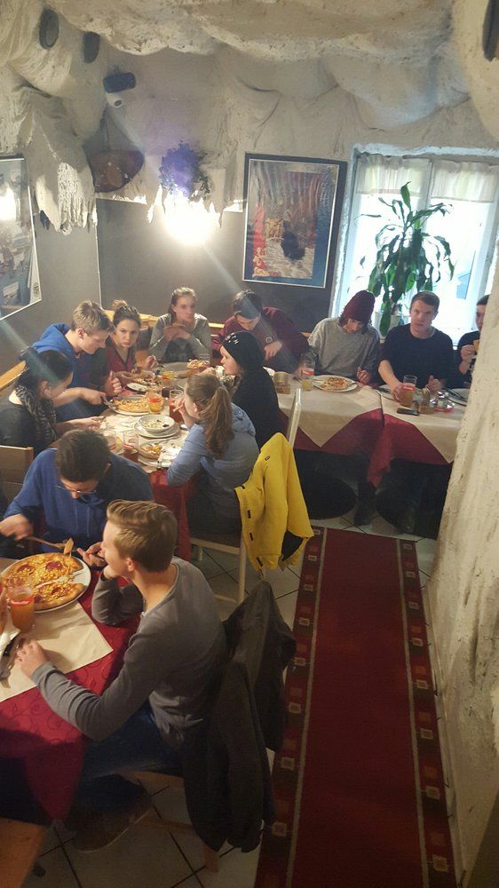 Gruppe von Menschen isst Pizza in einem gemütlichen Restaurant mit Höhlenwänden.