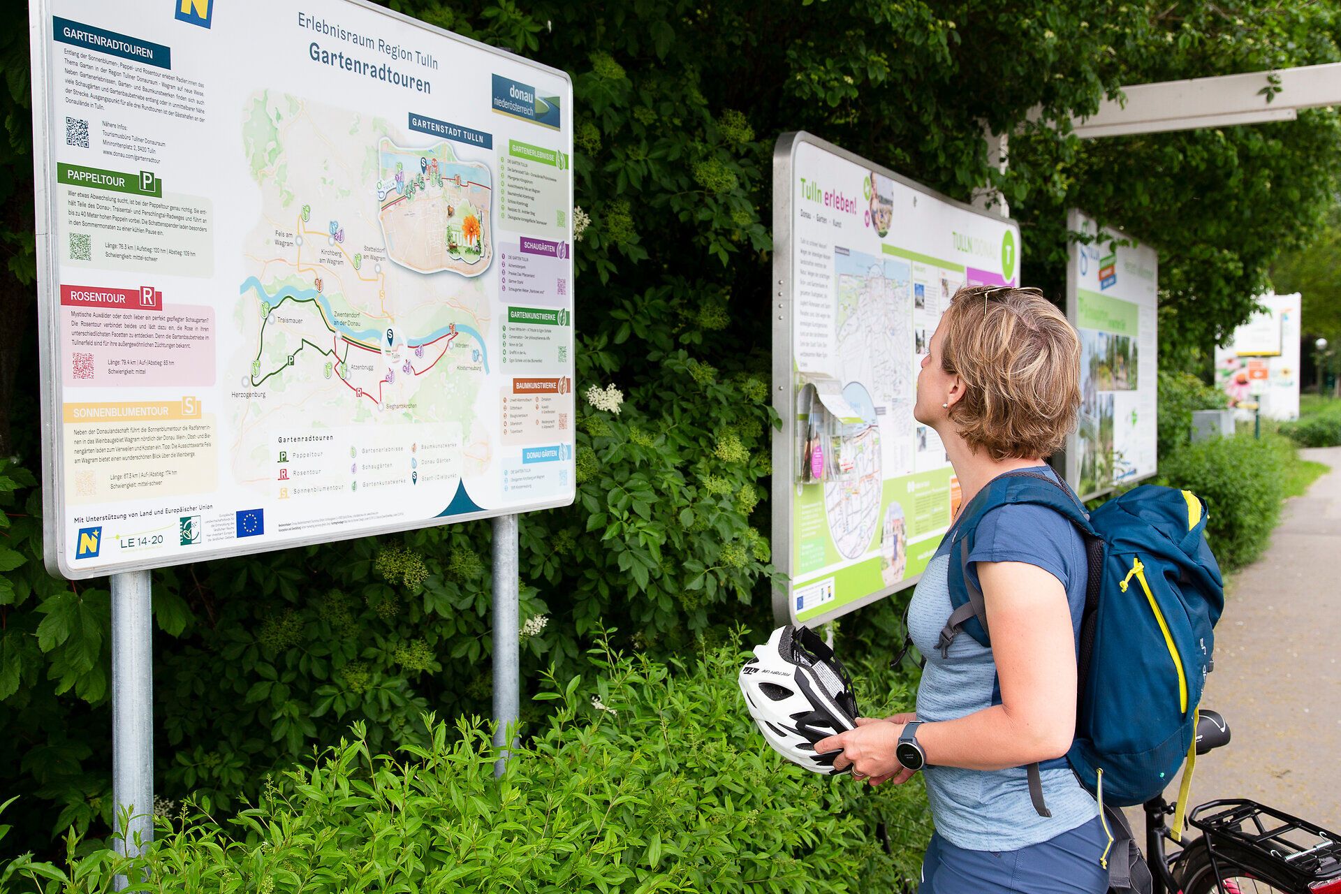 Frau liest auf Infotafel mit Helm in der Hand.