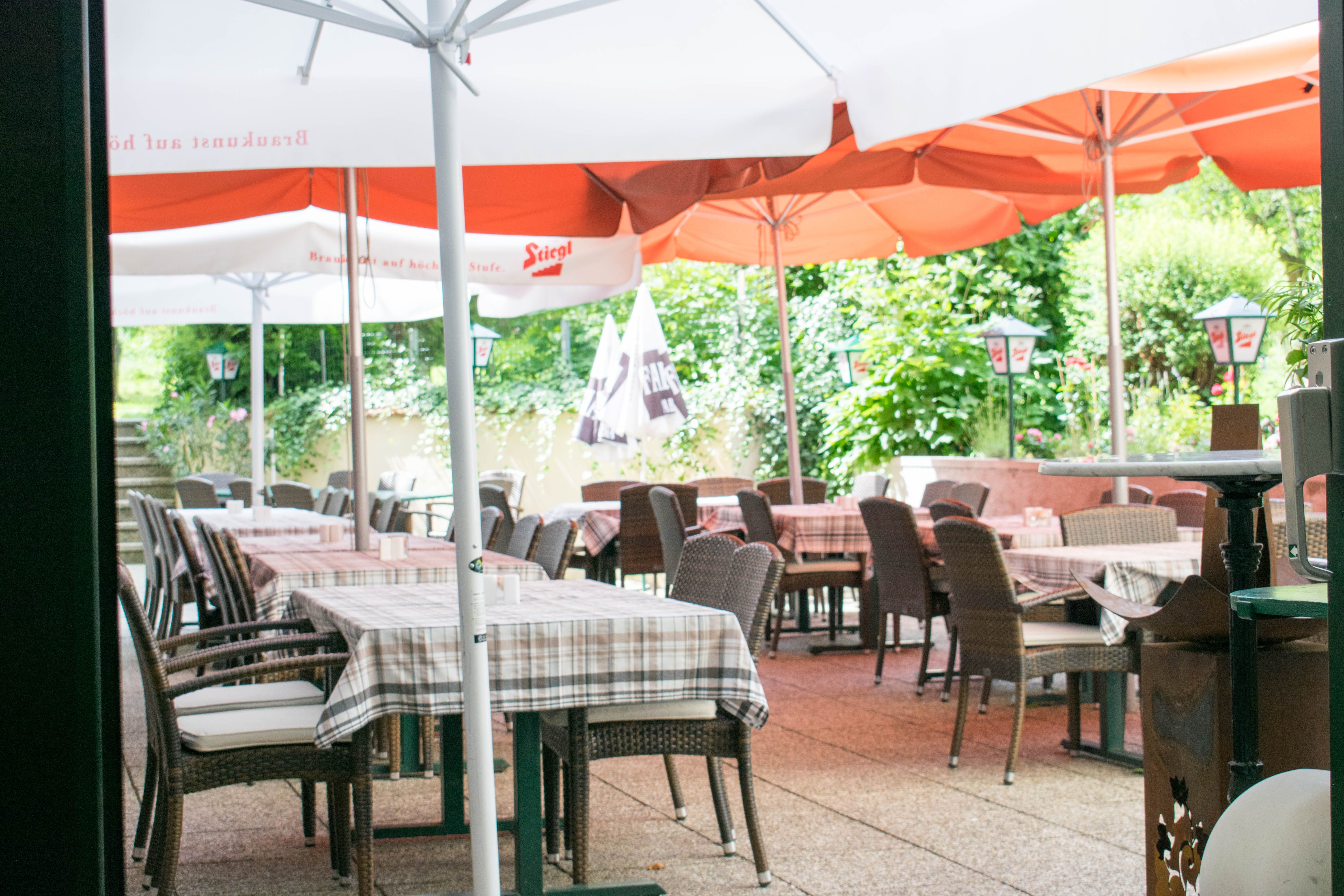 Außenbereich eines Cafés mit Tischen, Stühlen und Sonnenschirmen.