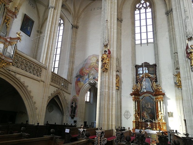 Innenansicht der Piaristenkirche mit Altar, Fresken und hohen Fenstern.