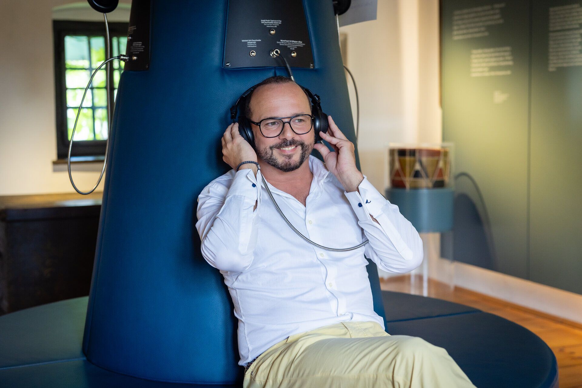 Der Museumsleiter, Michael Linsbauer, sitzt bei einer Hörstation und hat Kopfhörer auf.