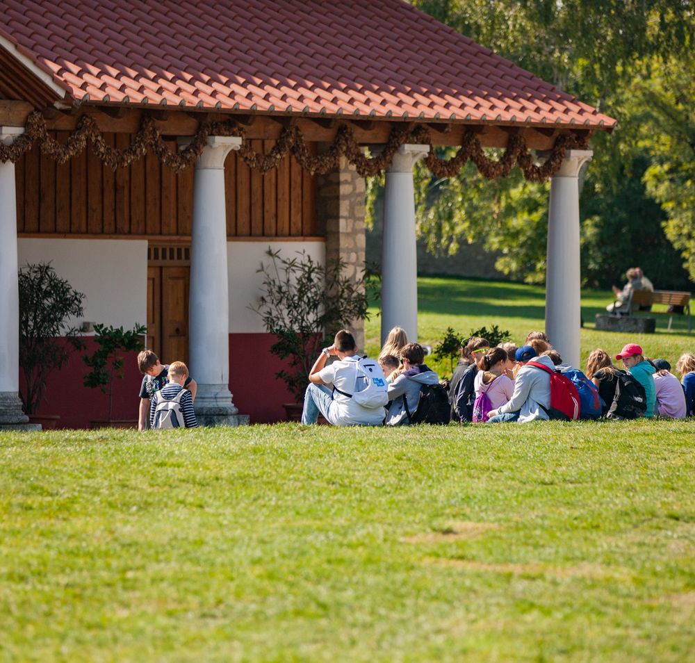 Schulklasse sitzt in der Wiese vor einer Römischen Therme in der Römerstadt Carnuntum