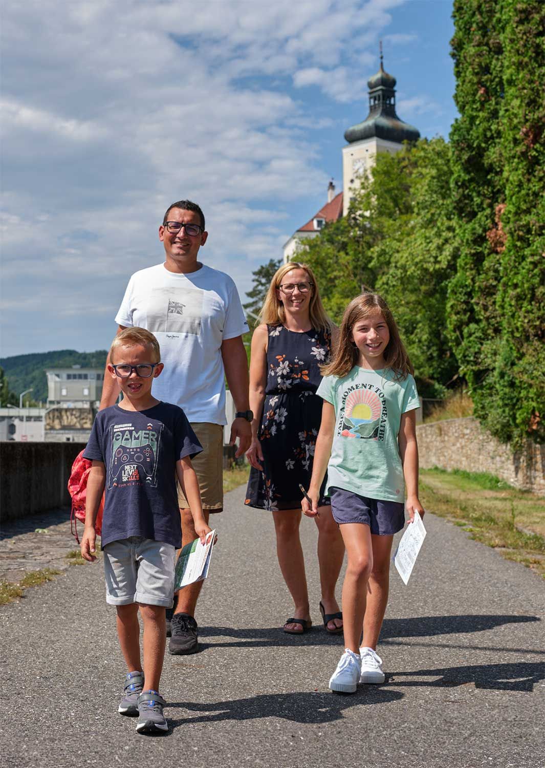 Egy család sétál egy ösvényen, a háttérben egy tornyos történelmi épület.