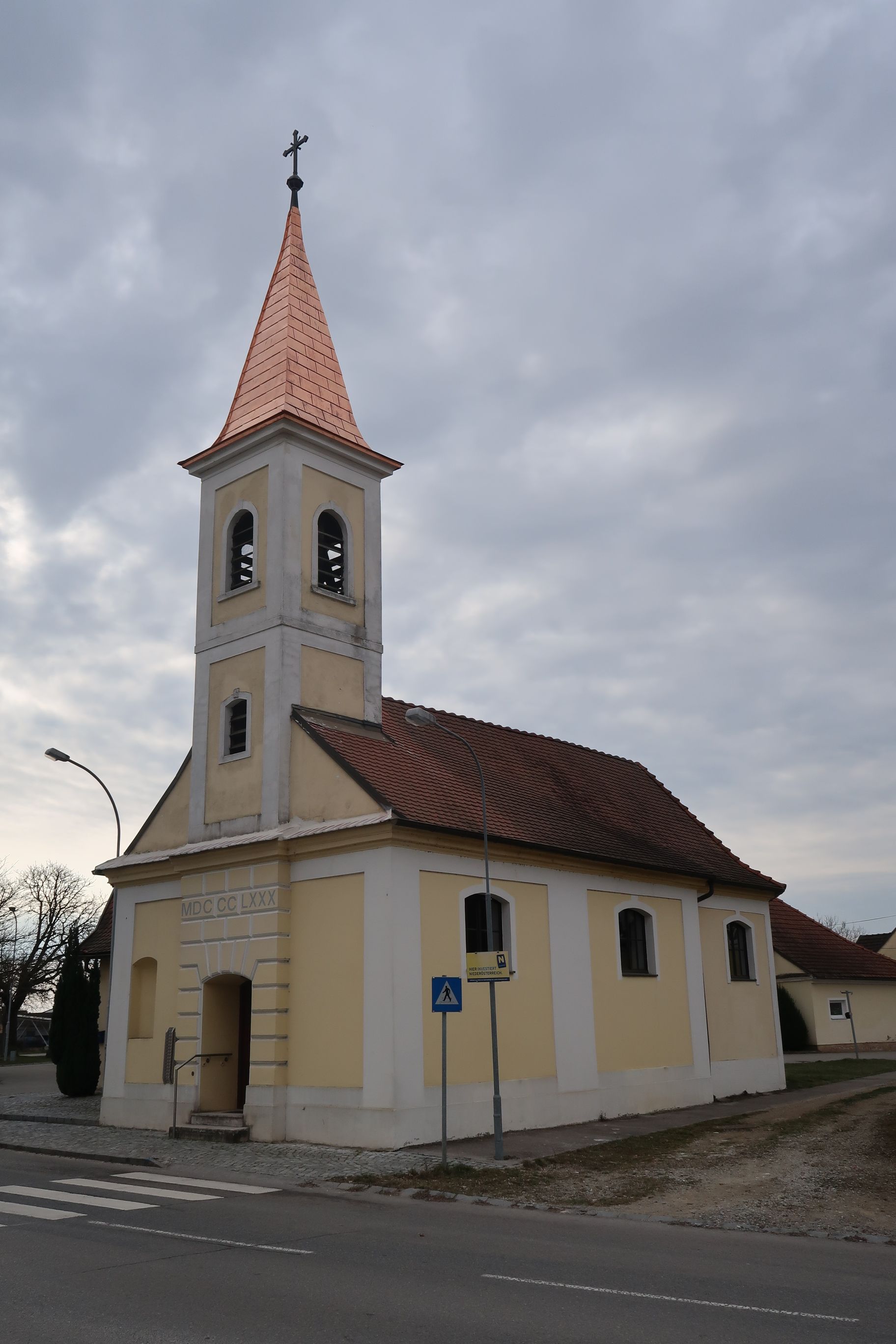 Kapelle Unterstockstall mit gelber Fassade und rotem Dach vor bewölktem Himmel.
