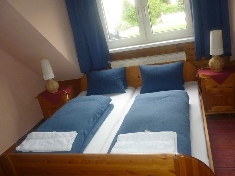 Ein gemütliches Doppelzimmer mit zwei Einzelbetten, blauer Bettwäsche und zwei Nachttischen mit Lampen, unter einem Fenster mit blauen Vorhängen.