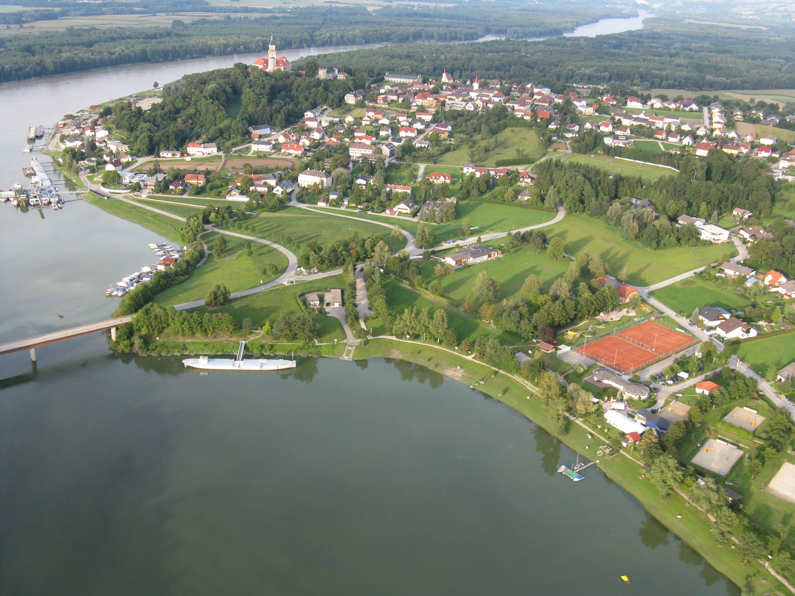 Luftaufnahme eines Wassersportzentrums mit Tennisplätzen, Bootsanlegern und einem Fluss.