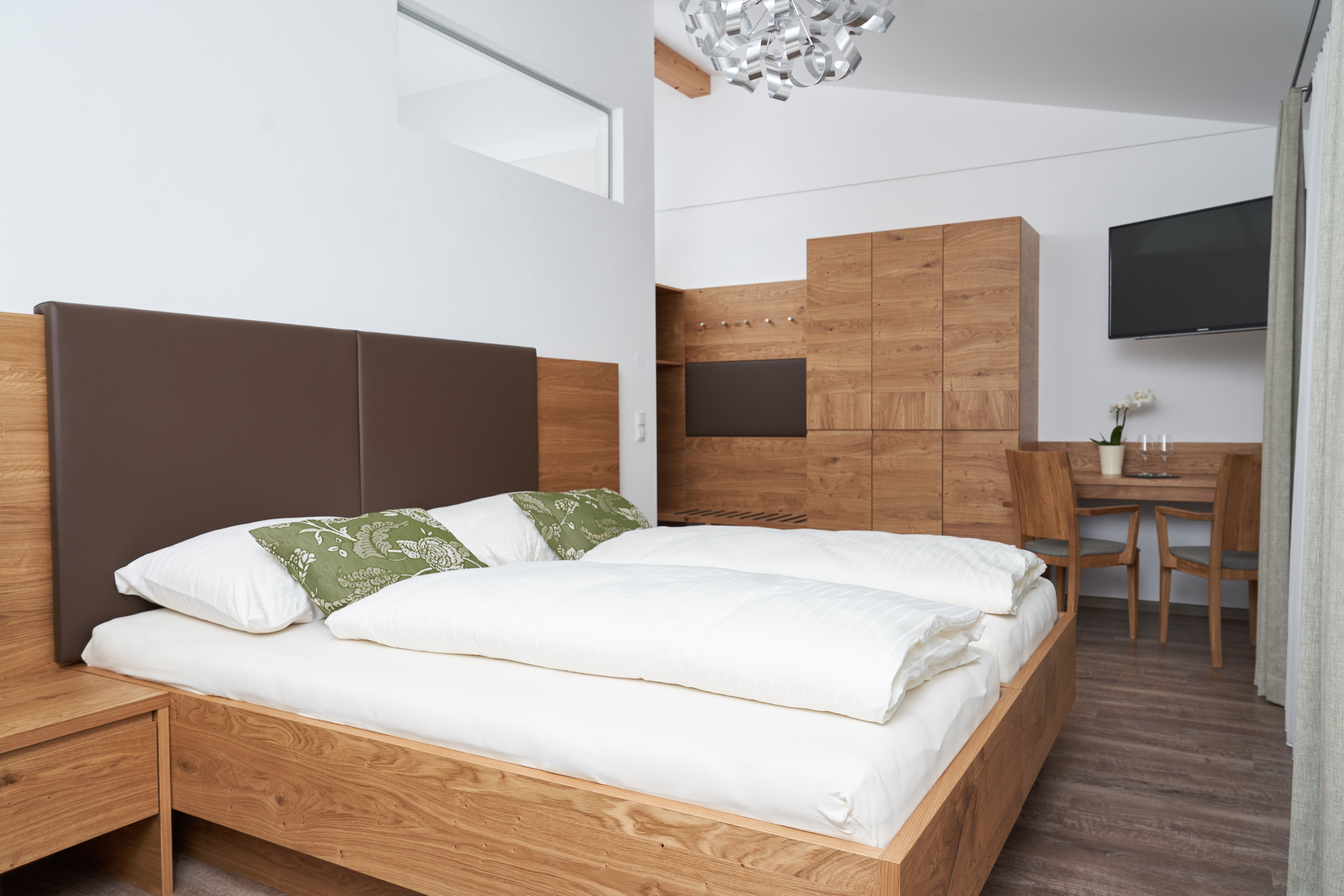 Modernes Schlafzimmer mit Holzmöbeln, Doppelbett, Tisch und Stühlen.