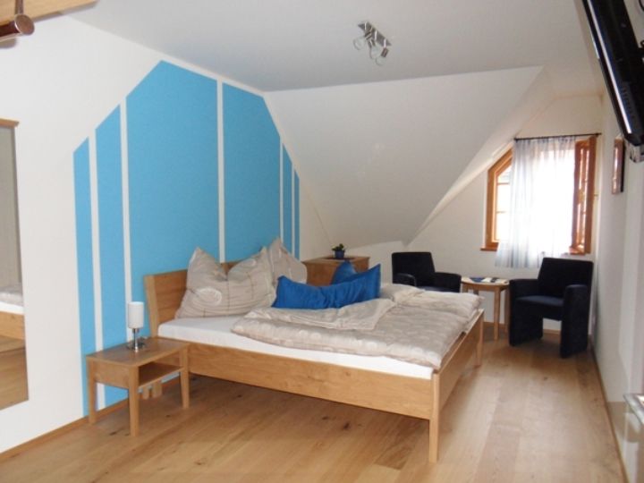 Ein Schlafzimmer mit blau-weißer Wand, Holzbett, zwei Sesseln und einem Fenster mit Vorhang.
