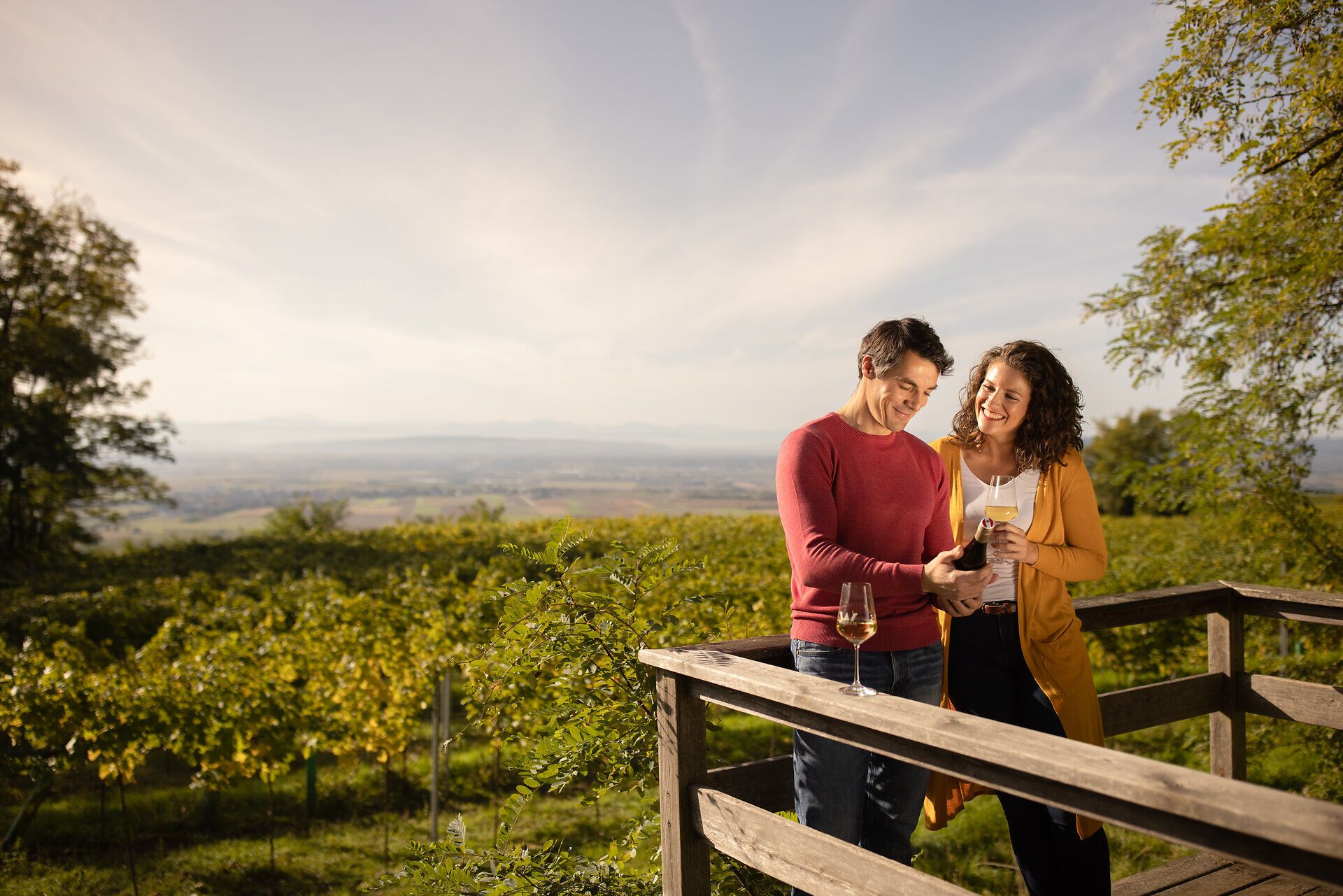 Ein Paar genießt einen romantischen Moment inmitten der sanften Hügel und Weinreben. Die goldene Abendsonne taucht die Landschaft in warmes Licht und schafft eine einladende Atmosphäre für eine unvergessliche Weinreise.
