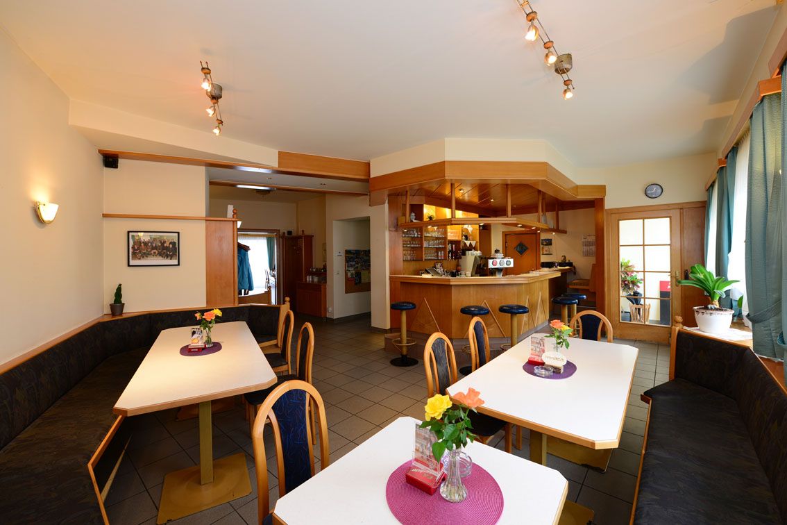 Innenansicht einer gemütlichen Gaststube mit Tischen, Stühlen und einer Bar.