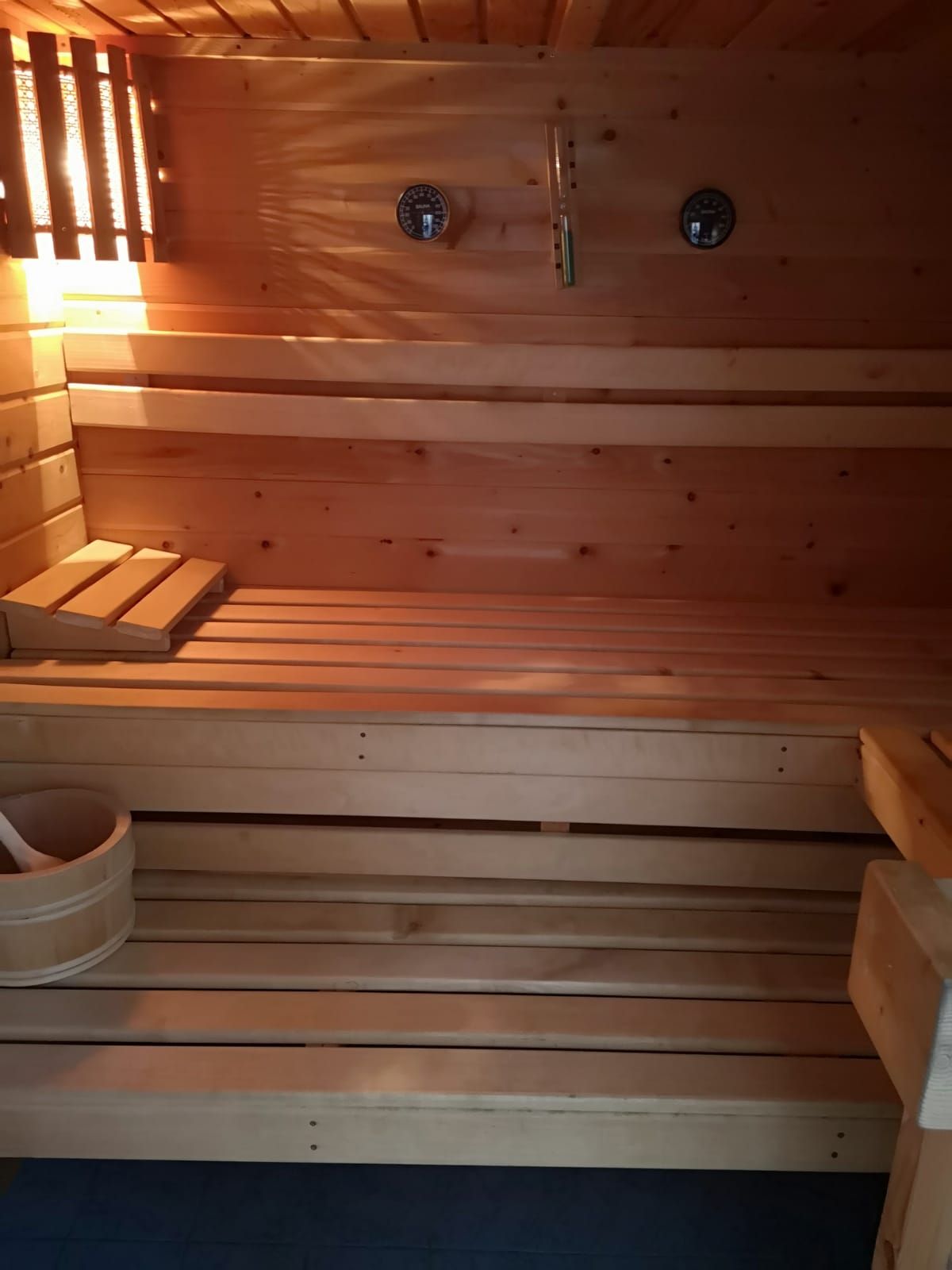 Innenansicht einer Holzsauna mit Bänken, Thermometer und Eimer.