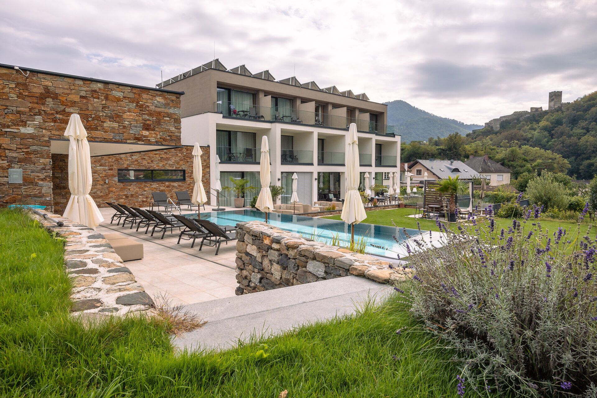 Umgeben von üppigem Grün und malerischen Ausblicken lädt das Boutiquehotel WEINSPITZ zu einem entspannten Aufenthalt ein. Die stilvollen Liegen am Pool versprechen erholsame Stunden unter der warmen Sonne, während die sanften Hügel im Hintergrund eine idyllische Kulisse bieten.