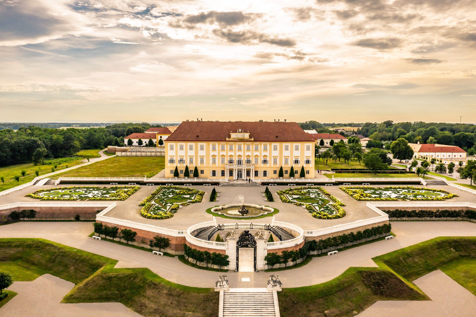 Die majestätische Fassade des Schlosses Hof strahlt im warmen Licht der Abendsonne und lädt zu einem Spaziergang durch die kunstvoll gestalteten Gärten ein. Hier, wo Geschichte und Natur harmonisch verschmelzen, können Besucher die Schönheit der Landschaft und die Pracht der Architektur genießen.