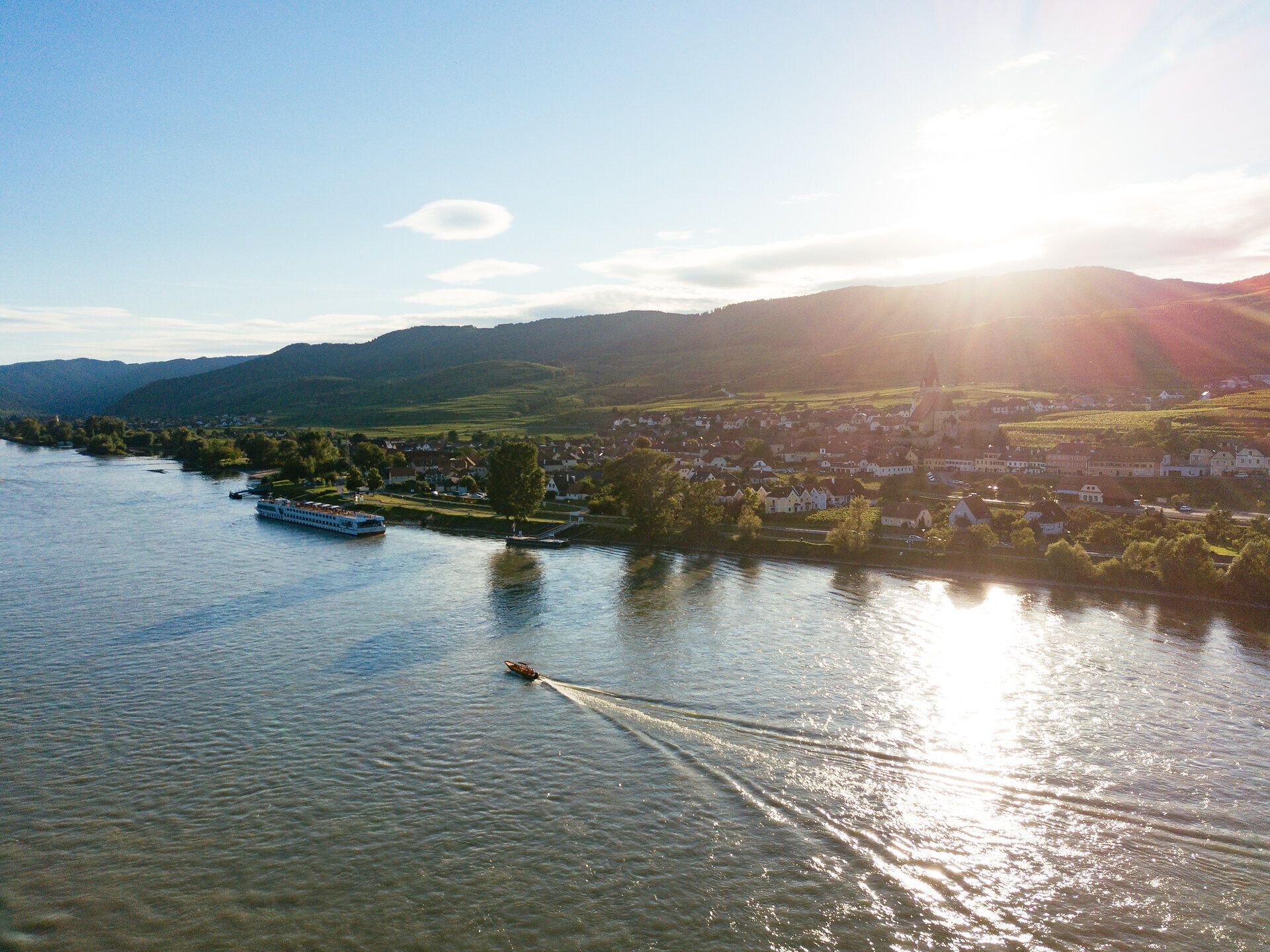 Die sanften Hügel der Wachau erstrahlen im warmen Licht der Abendsonne, während die Donau friedlich dahinfließt. Ein Boot gleitet über das Wasser und bietet einen atemberaubenden Blick auf die malerische Landschaft, die von Weinbergen und charmanten Dörfern geprägt ist.