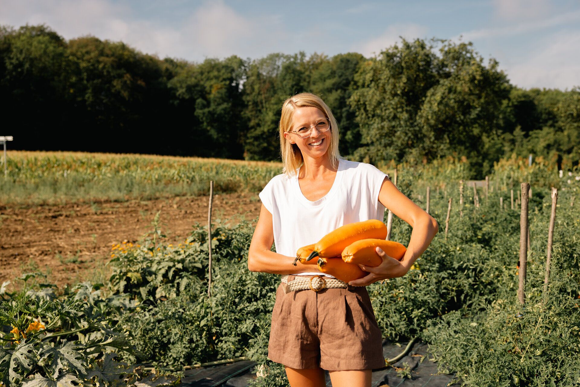 Frau hält mehrere gelbe Zucchini auf einem Feld.