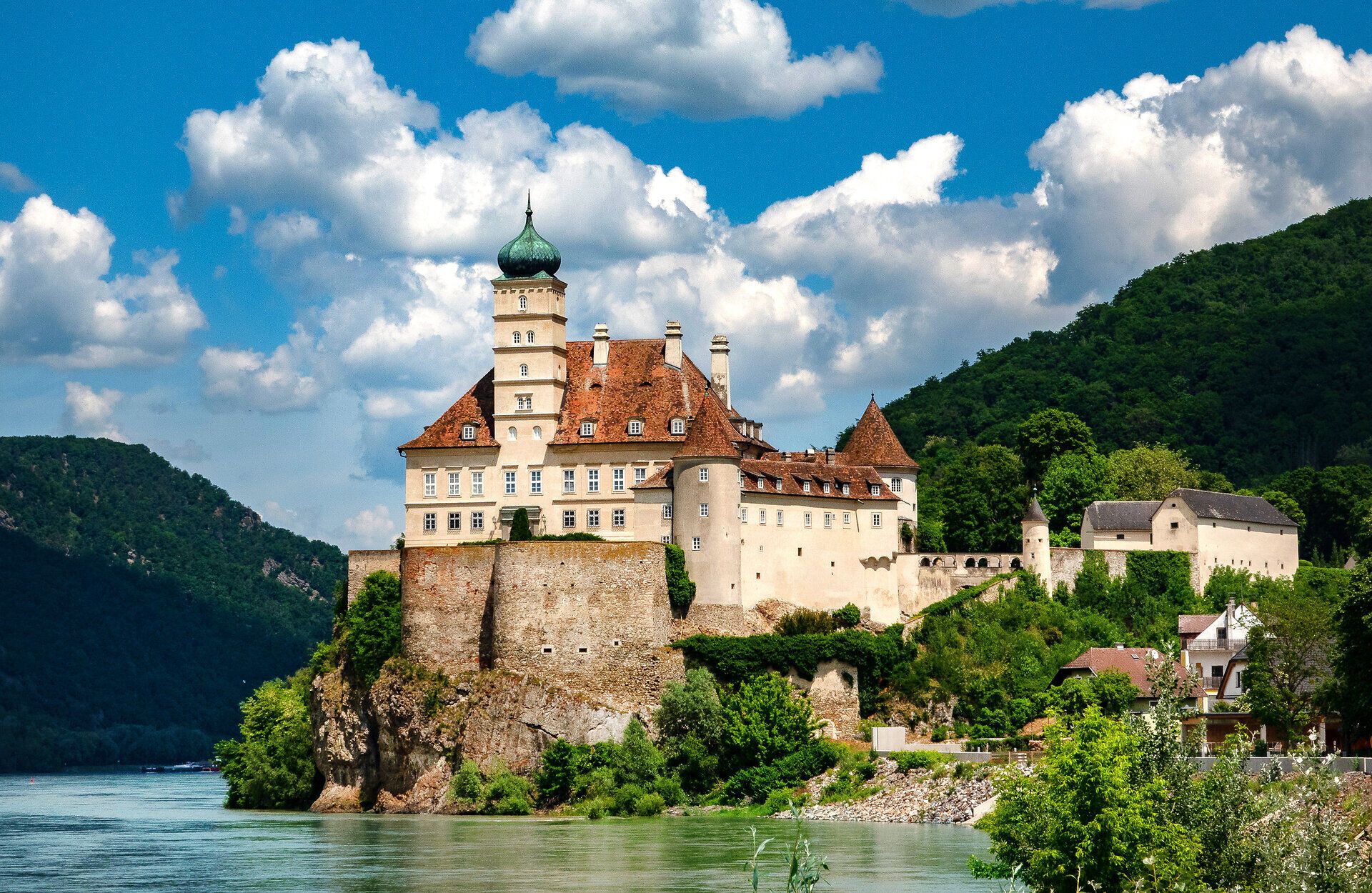 Das majestätische Schloss thront malerisch über dem ruhigen Fluss, umgeben von üppigem Grün und sanften Hügeln. An warmen Sommertagen lädt die idyllische Kulisse dazu ein, die Schönheit der Natur zu genießen und die Seele baumeln zu lassen.