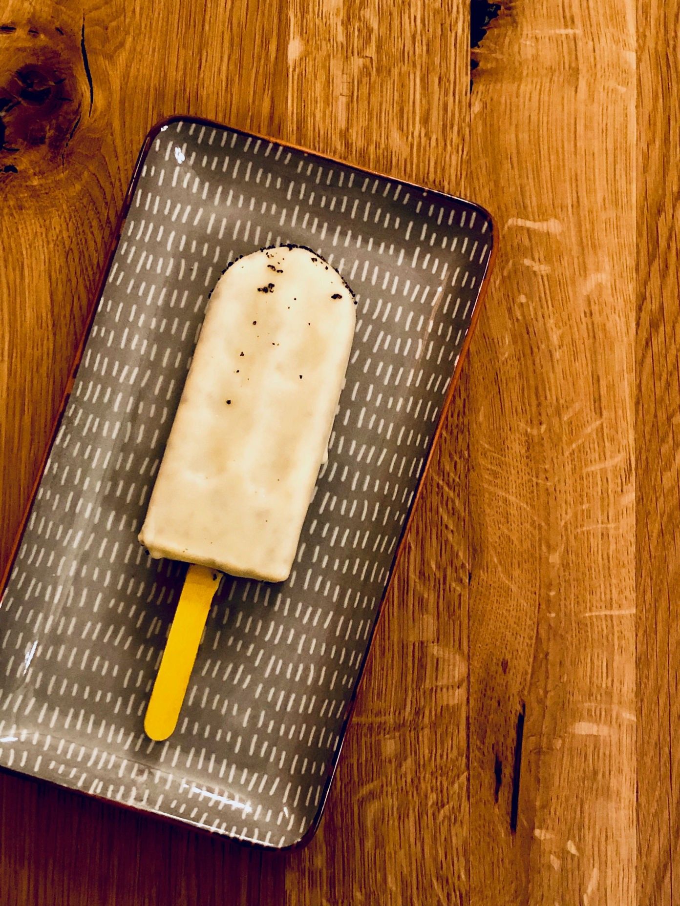 Ein Eis am Stiel auf einem gemusterten Teller auf einem Holztisch.