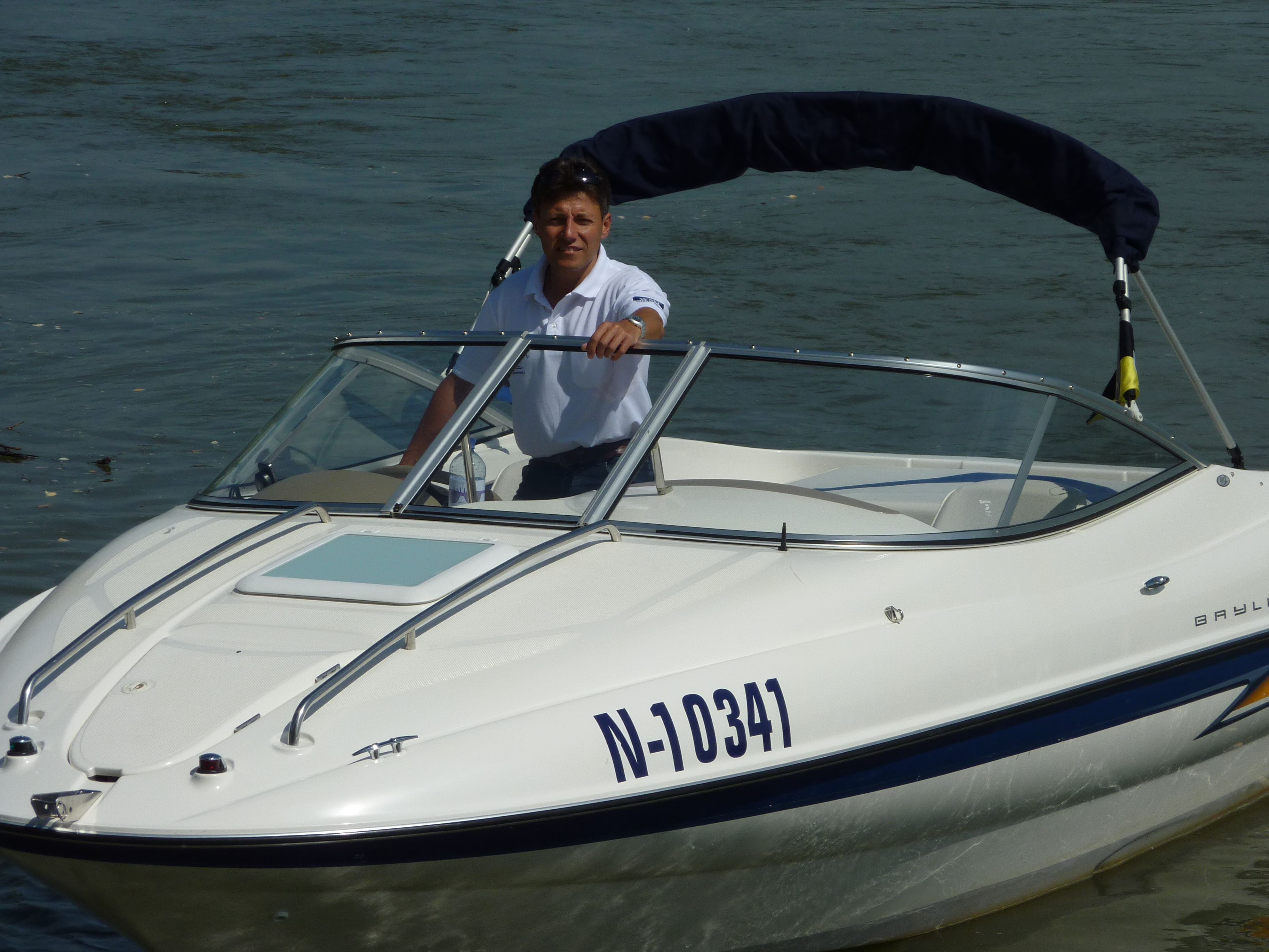 Ein Mann steht auf einem weißen Motorboot, das am Wasser liegt.