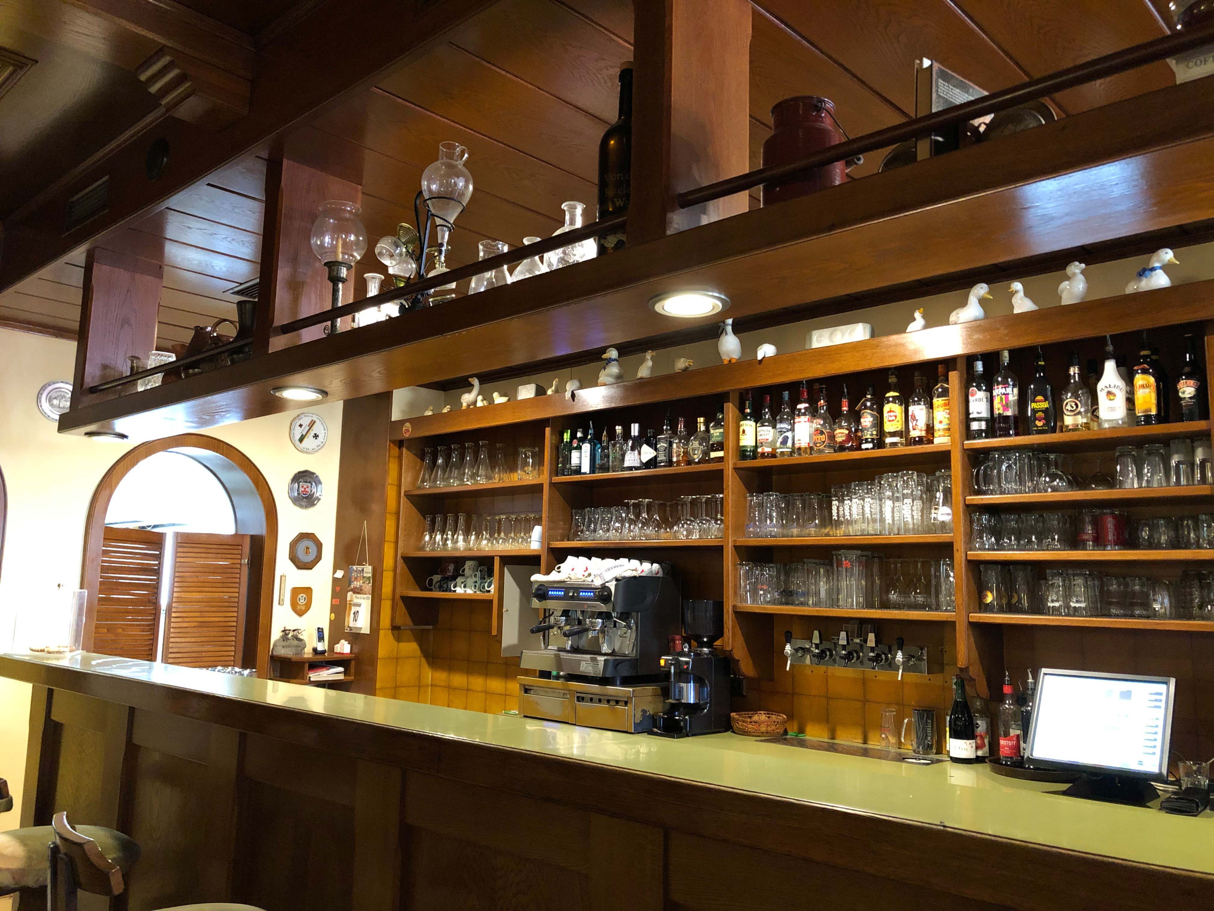 Innenansicht einer Bar mit Holzregalen, Gläsern und Flaschen.