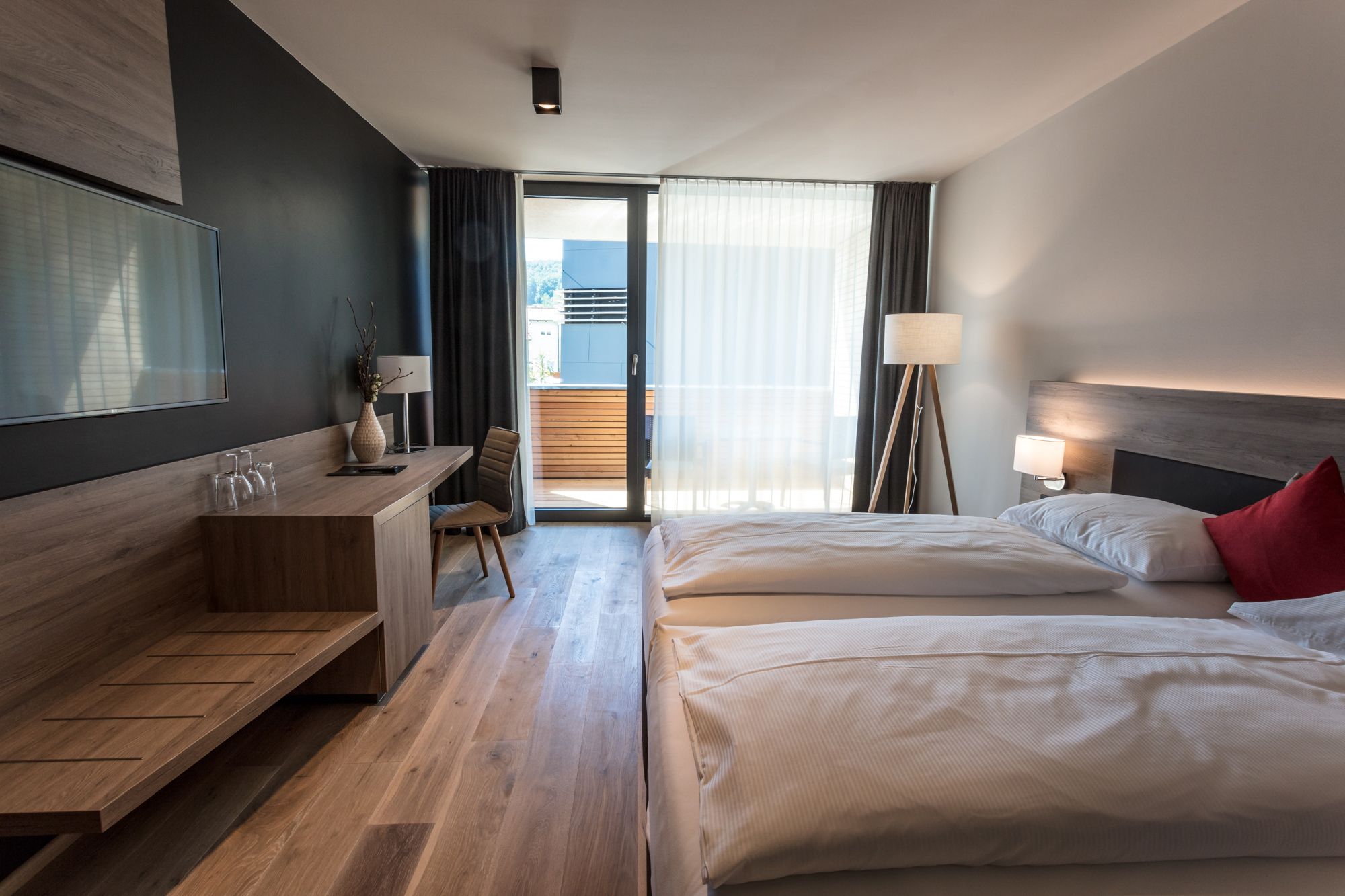 Modernes Hotelzimmer mit zwei Betten, Schreibtisch und Balkon.