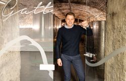 Junger Mann in dunklem Pullover und Jeans schaut aus einer halb geöffneten Glastür heraus.