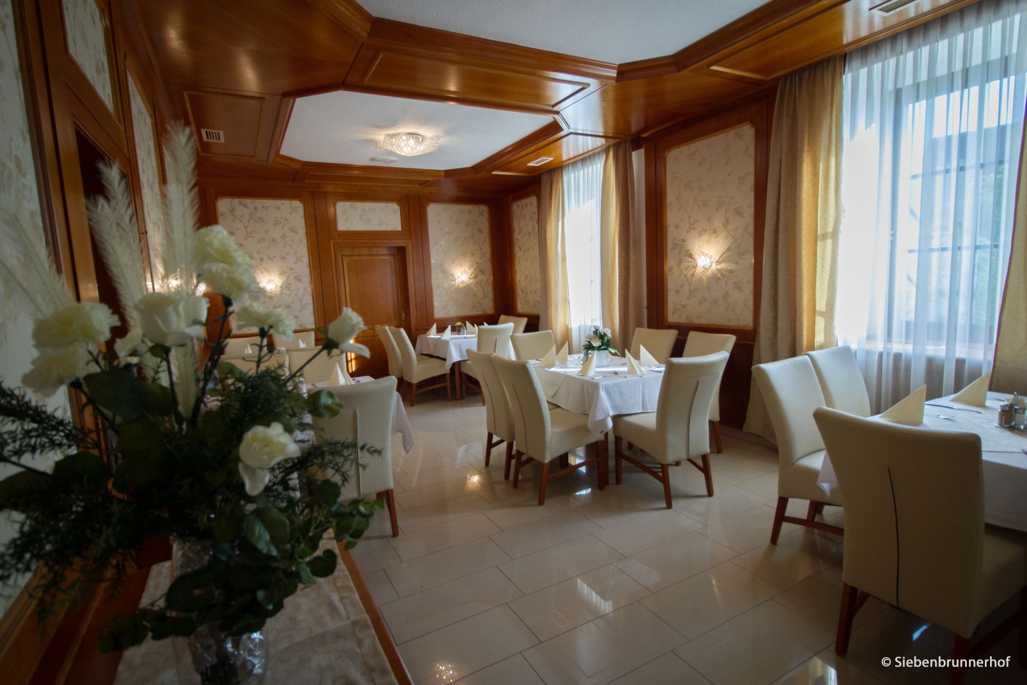 Elegant dining room with laid tables, white chairs and flower arrangements.