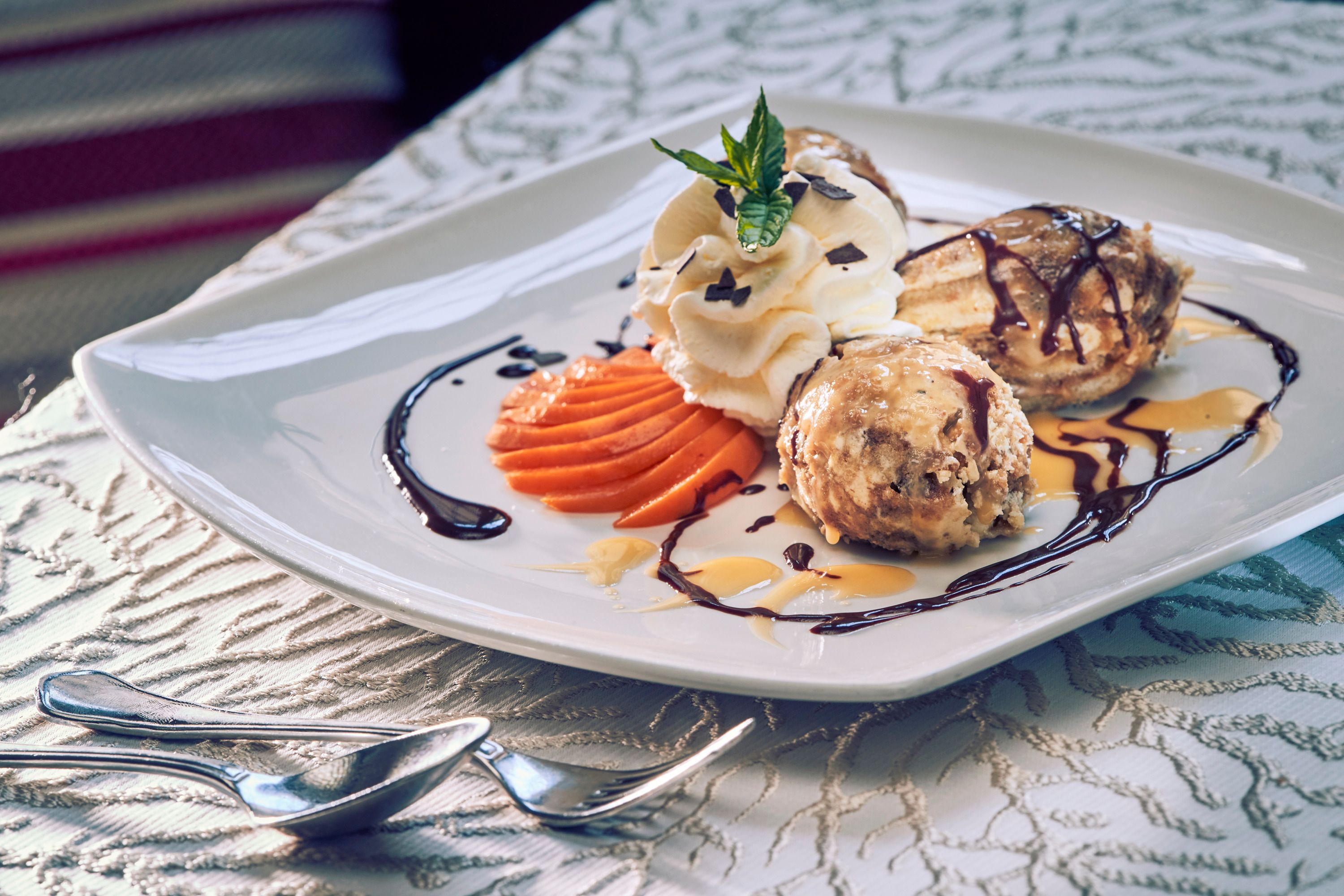 Ein Dessertteller mit Malakoffnockerl, Sahne, Schokoladensauce und dekorativen Früchten.