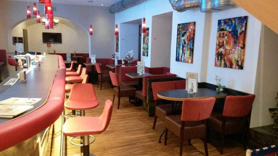 Innenansicht eines modernen Cafés mit roten Stühlen und Barhockern.