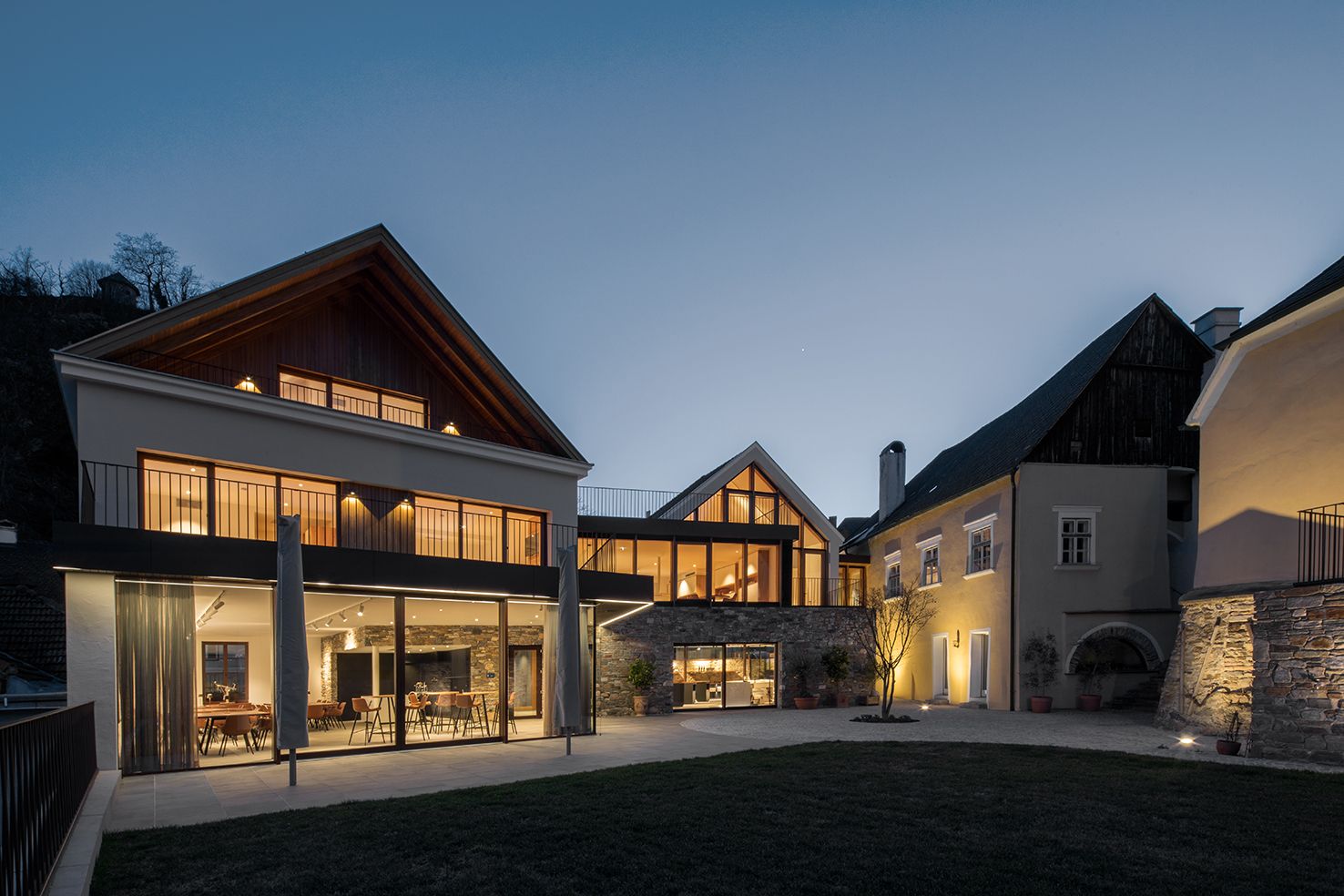 Moderne Gebäudes des Mauritiushofes mit großen Fenstern in der Abenddämmerung, beleuchtet von warmem Licht.