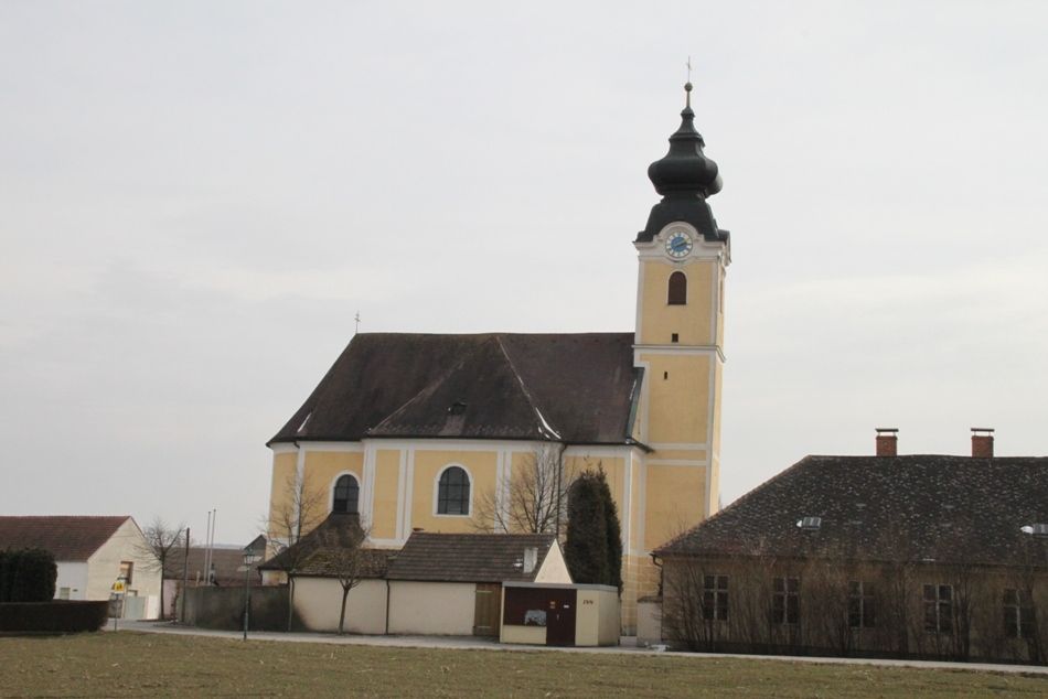 Gelbe Kirche mit Turm und Uhr in Langenrohr, umgeben von Gebäuden und Bäumen.