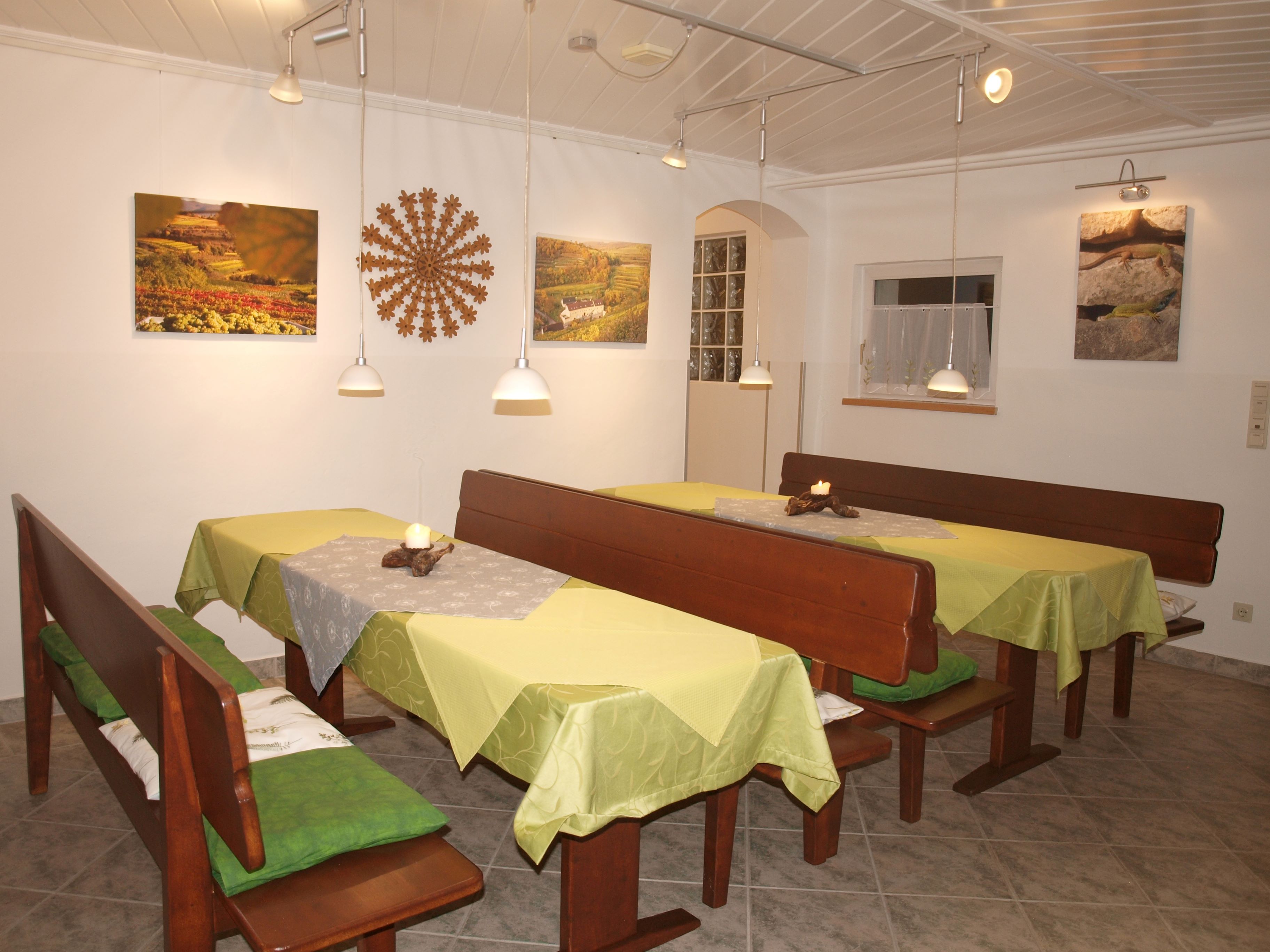 Ein gemütlicher Frühstücksraum mit Holzbänken, grünen Tischdecken und Wanddekorationen.