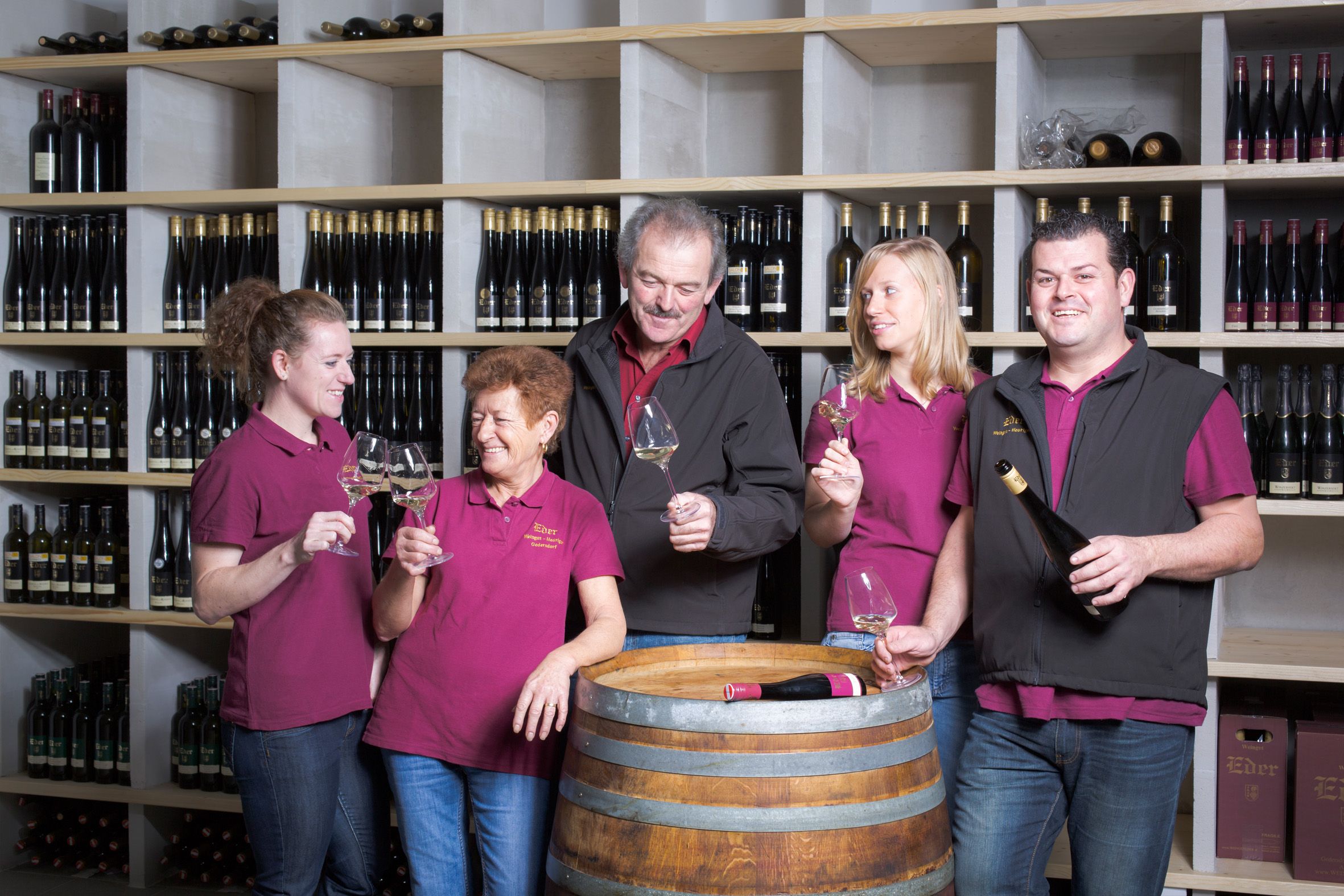 Fünf Personen in einem Weinkeller stoßen mit Weingläsern an.