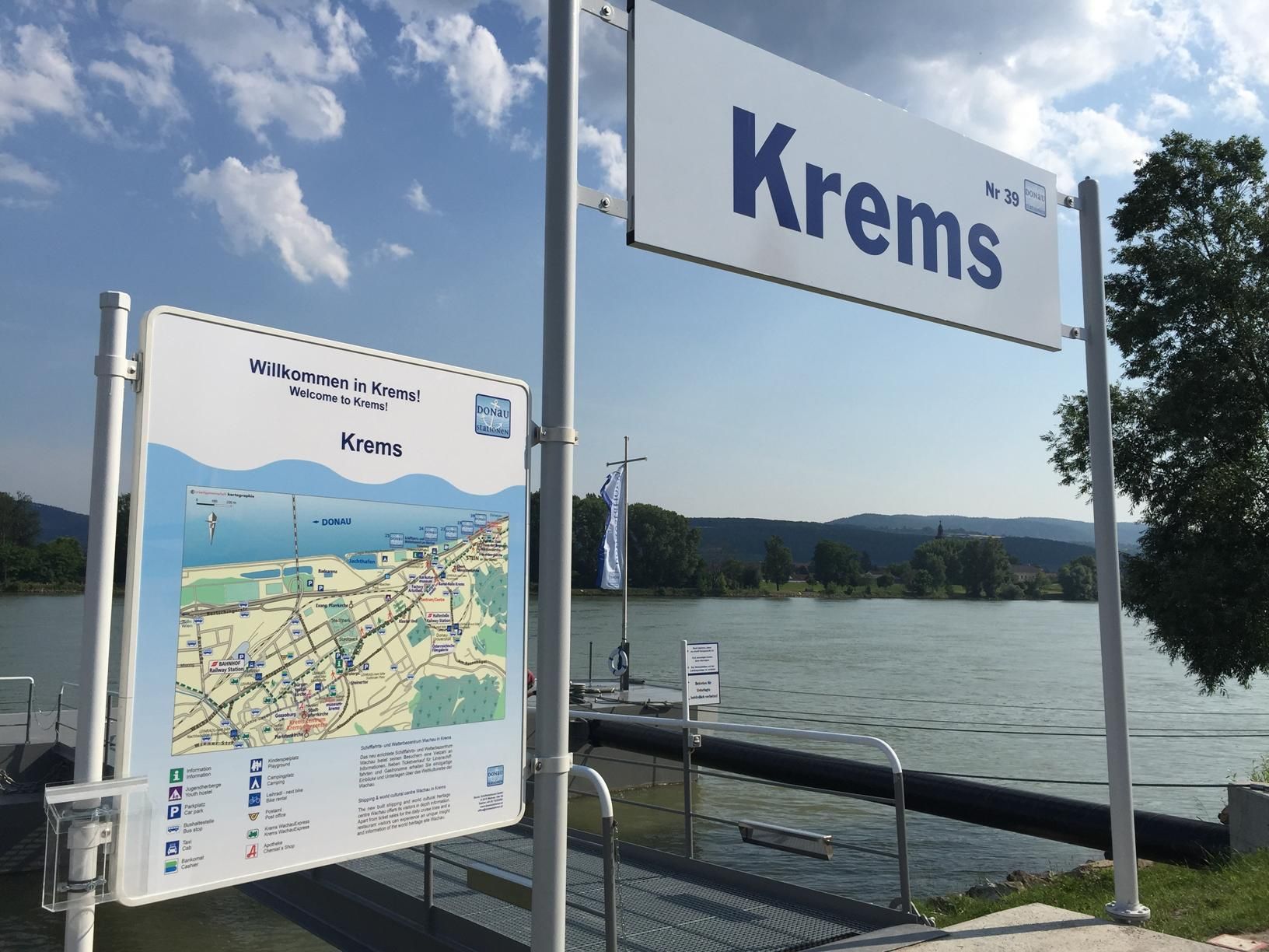 Anlegesteg in Krems mit Willkommensschild und Karte, Fluss im Hintergrund.
