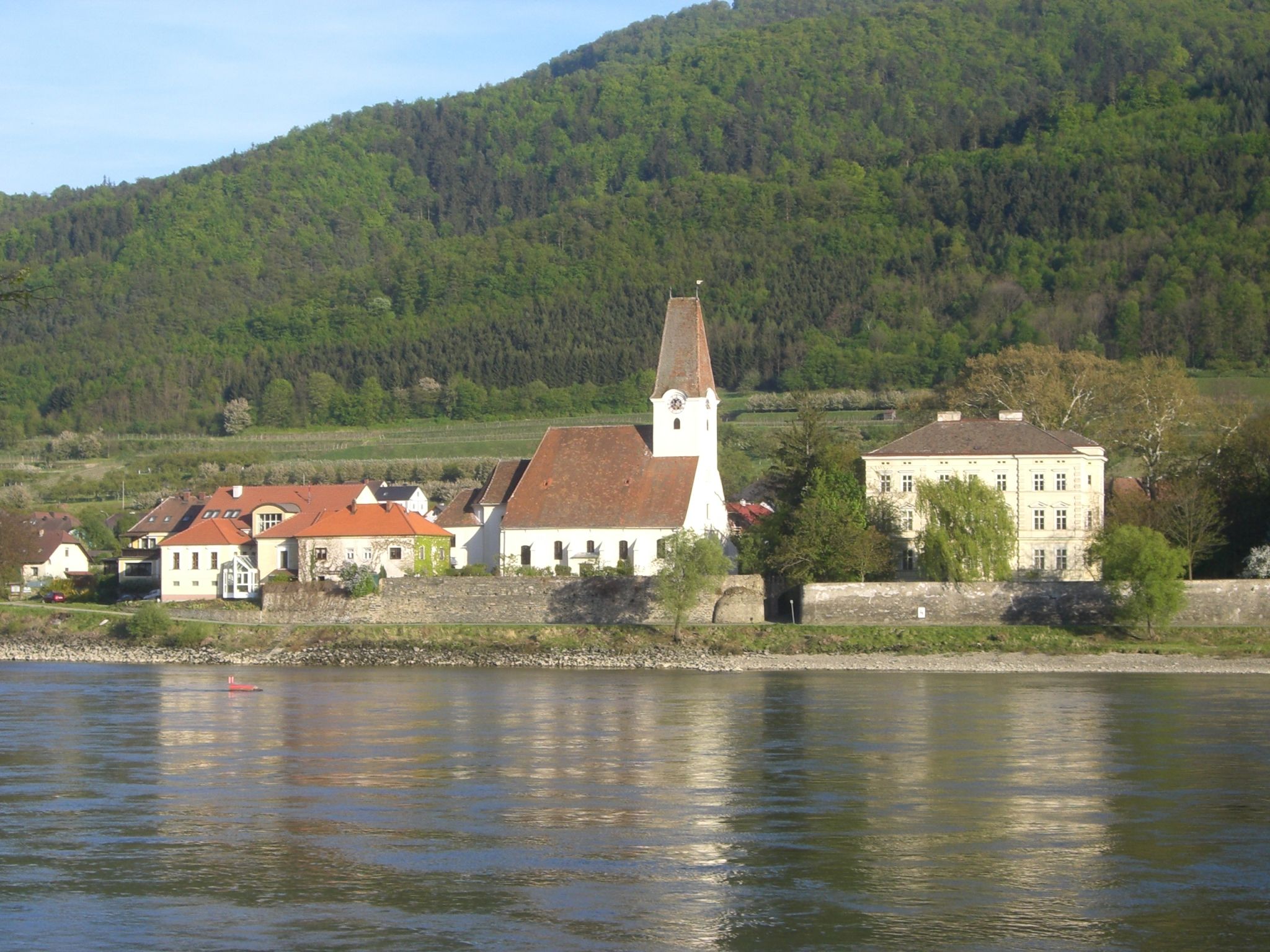 Schloss Hofarnsdorf und Kirche an der Donau mit bewaldetem Hügel im Hintergrund.