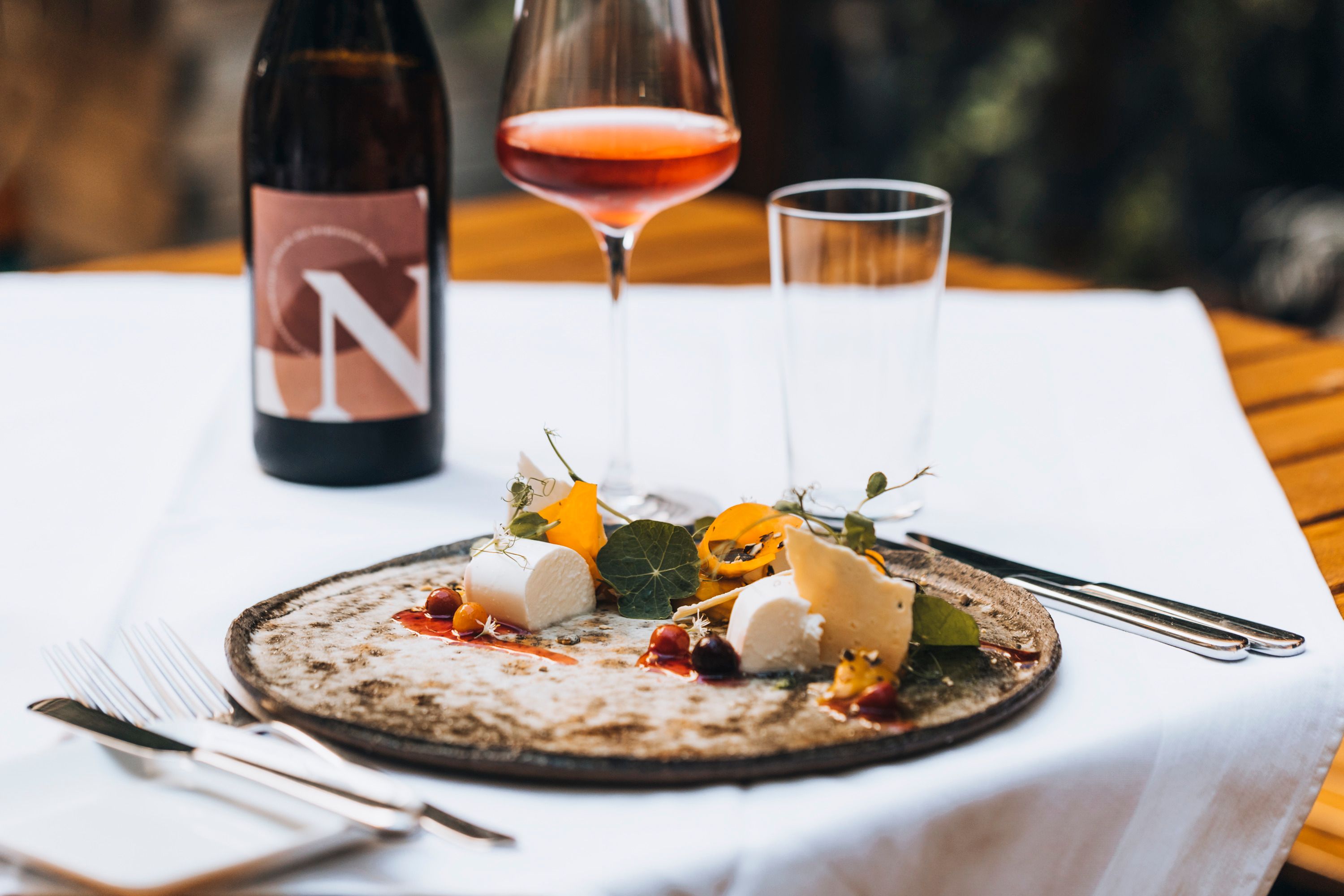 Ein Teller mit Käse und Garnitur, ein Glas Roséwein und eine Weinflasche auf einem Tisch.