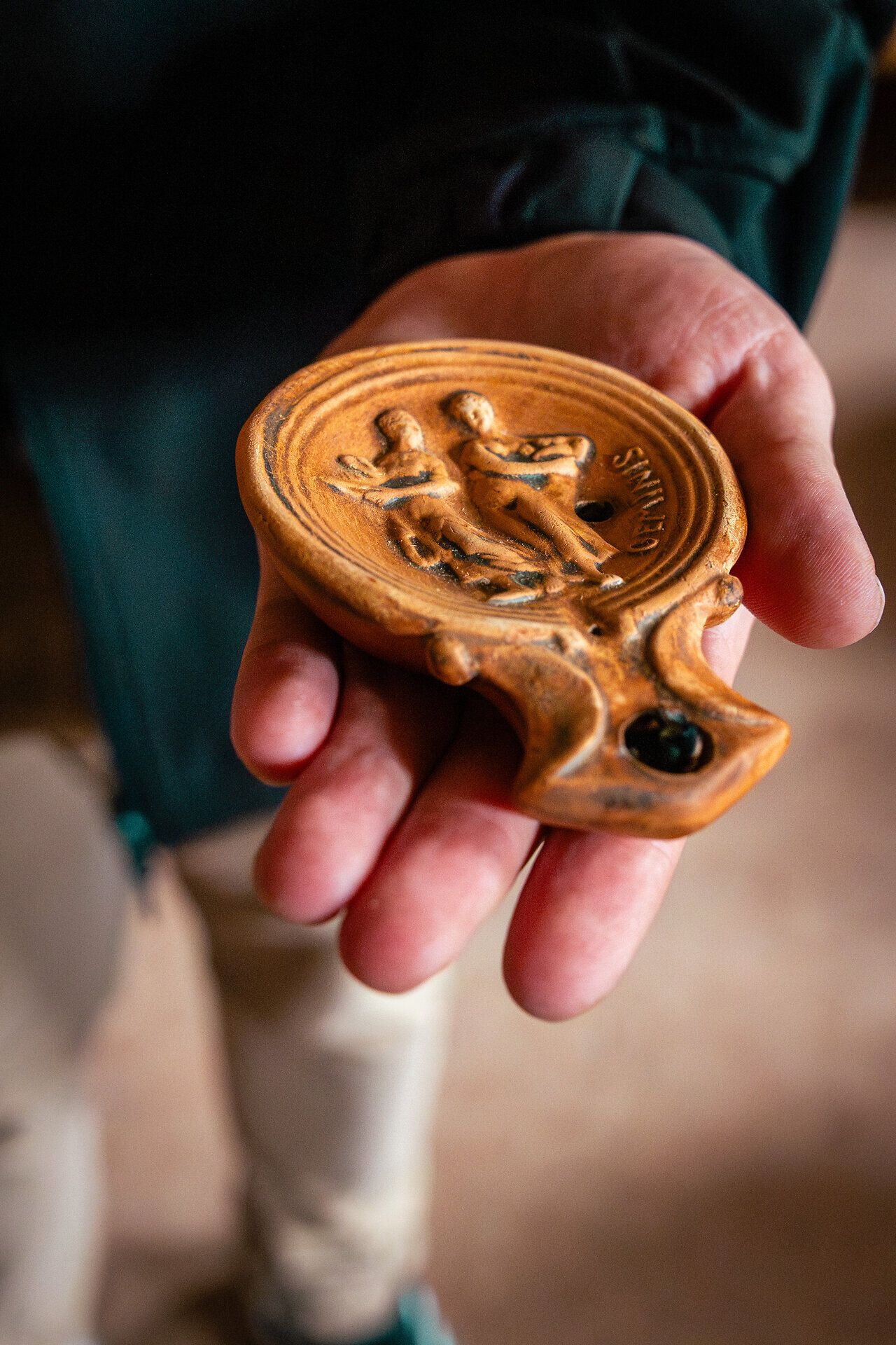 Eine Hand hält eine römische Öllampe aus Ton.