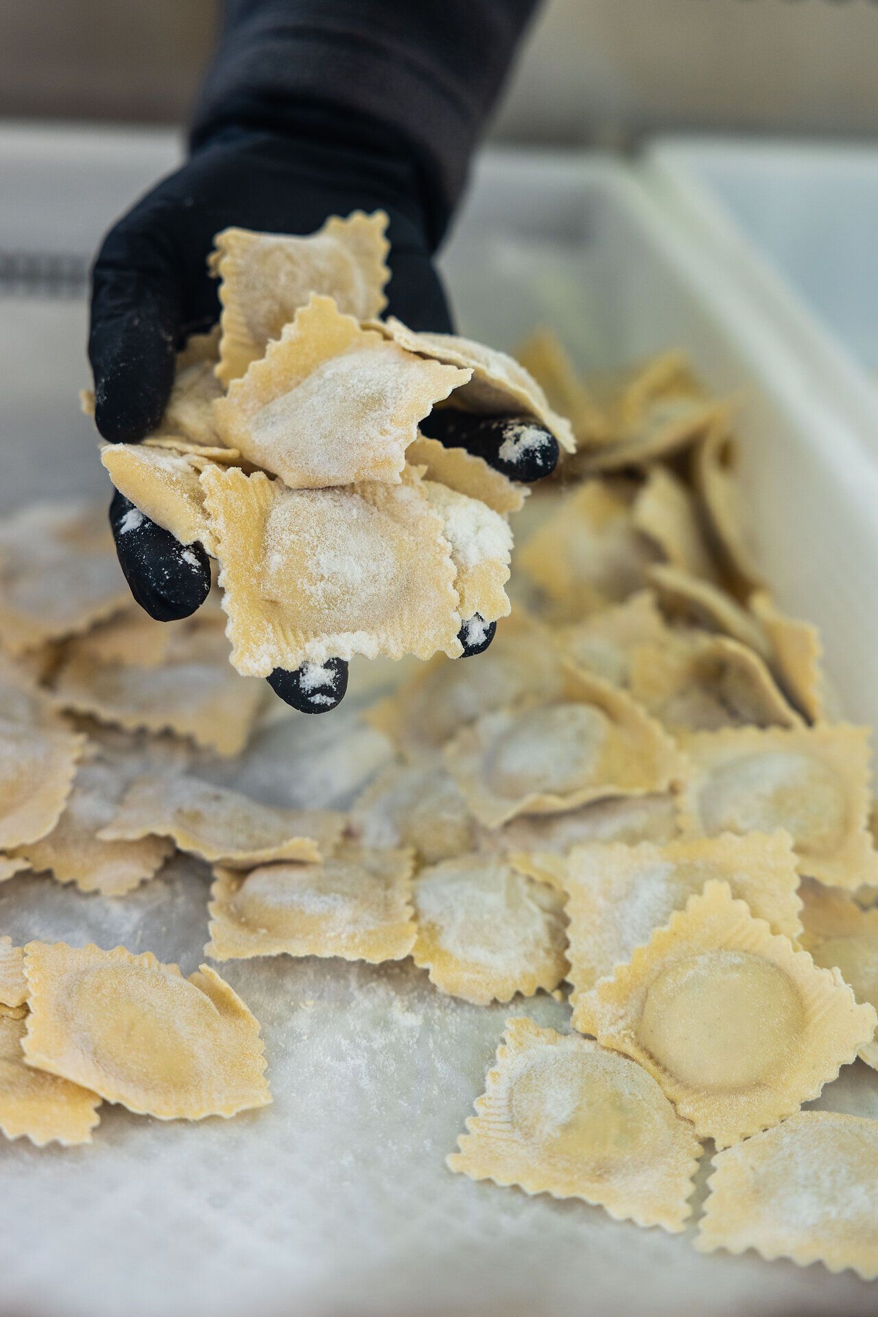 Ein Hand mit schwarzem Handschuh hält Raviolli in die Kamera.