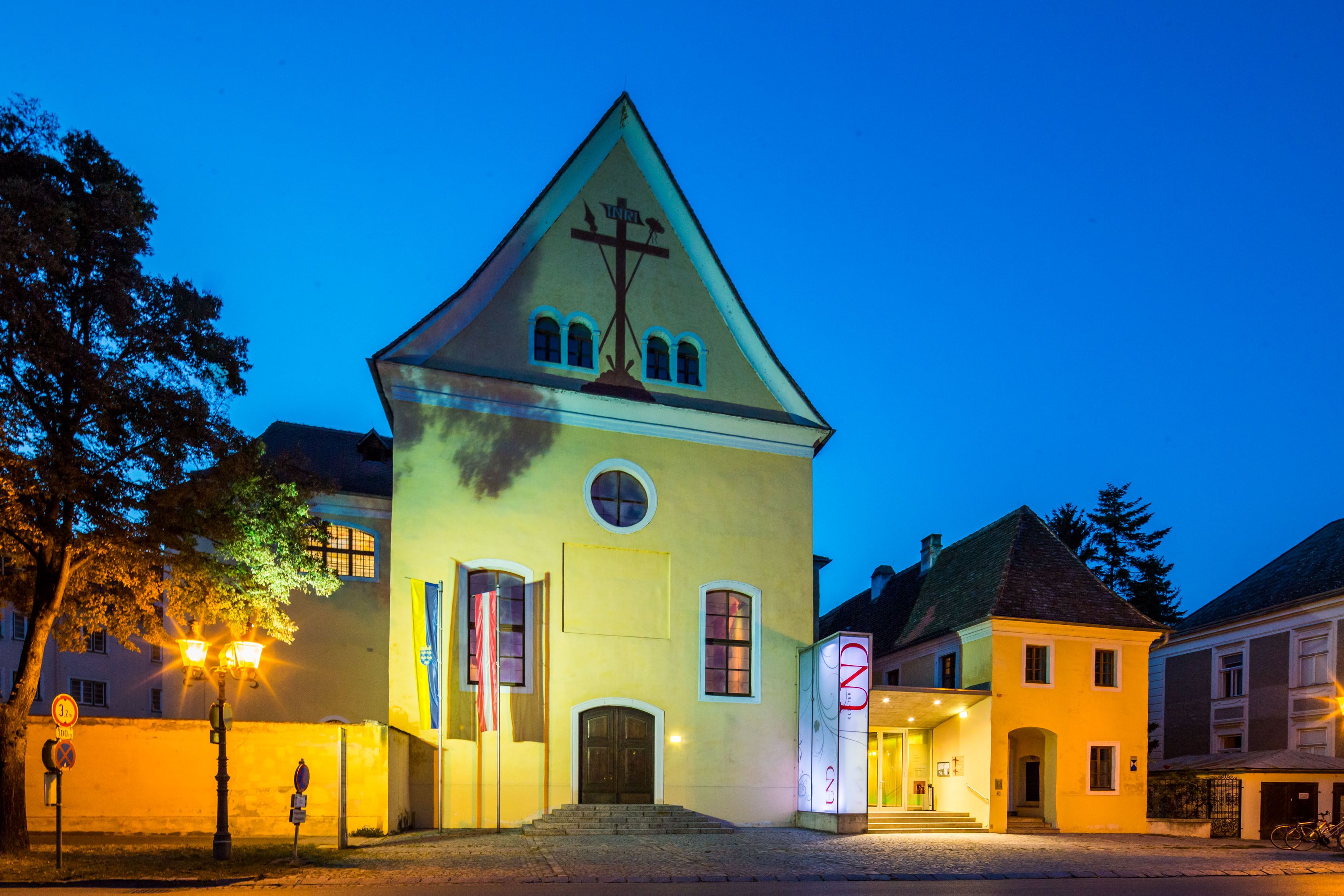Gelbes Gebäude mit Kreuzsymbol, beleuchtet bei Nacht.