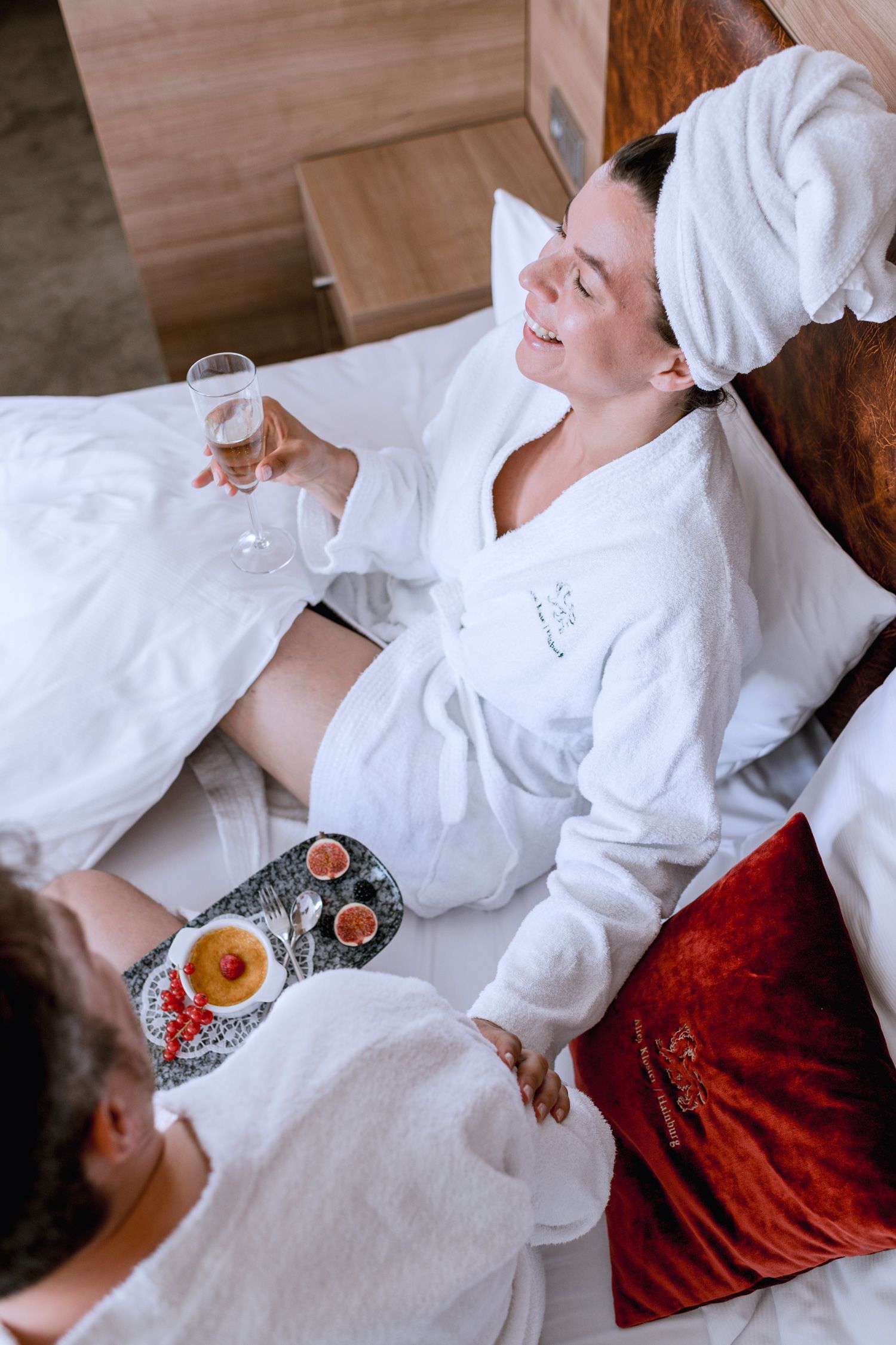 Zwei Personen im Bademantel frühstücken im Bett mit Sekt und Dessert.