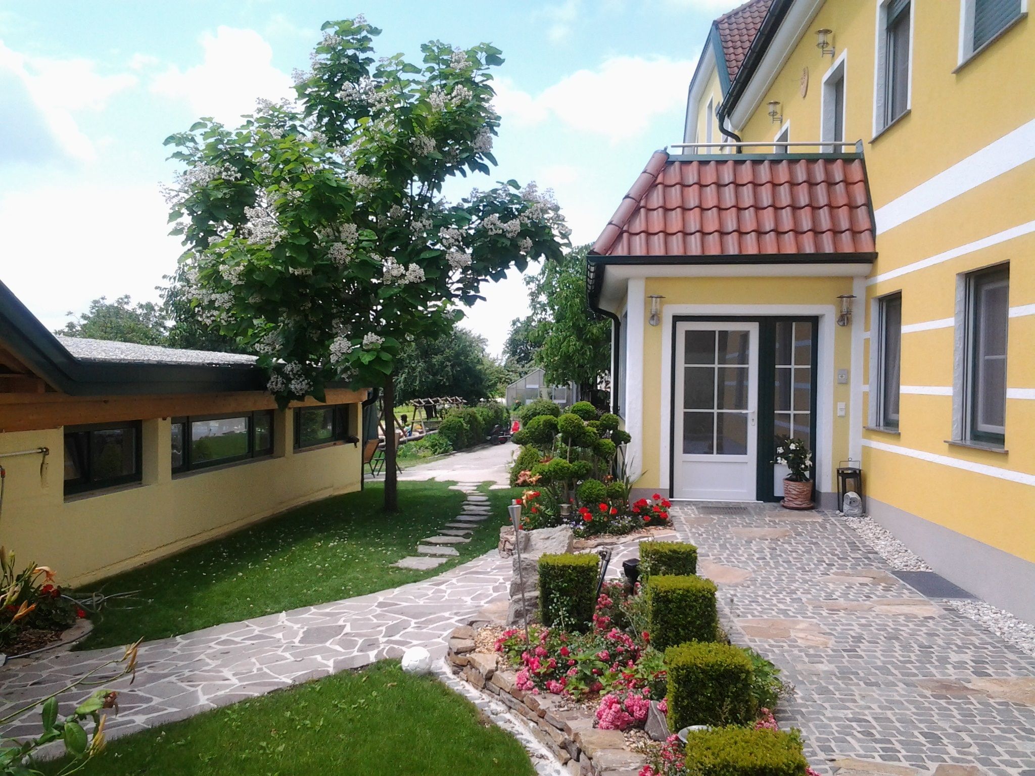Eingang eines gelben Gebäudes mit gepflegtem Garten und gepflastertem Weg.