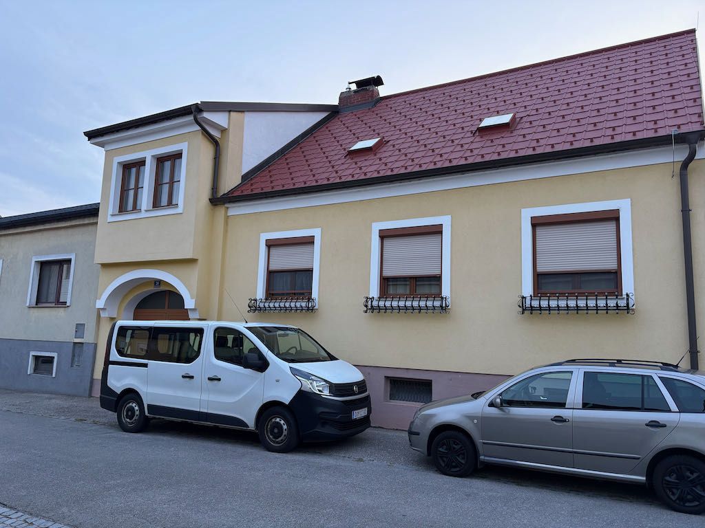 Dvě auta zaparkovaná před žlutým domem s červenou střechou.