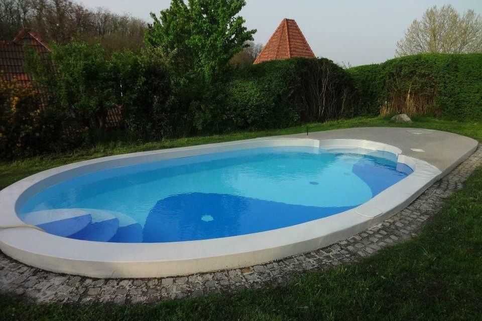 Ein ovaler Pool im Garten mit blauer Wasseroberfläche, umgeben von Rasen und Büschen.