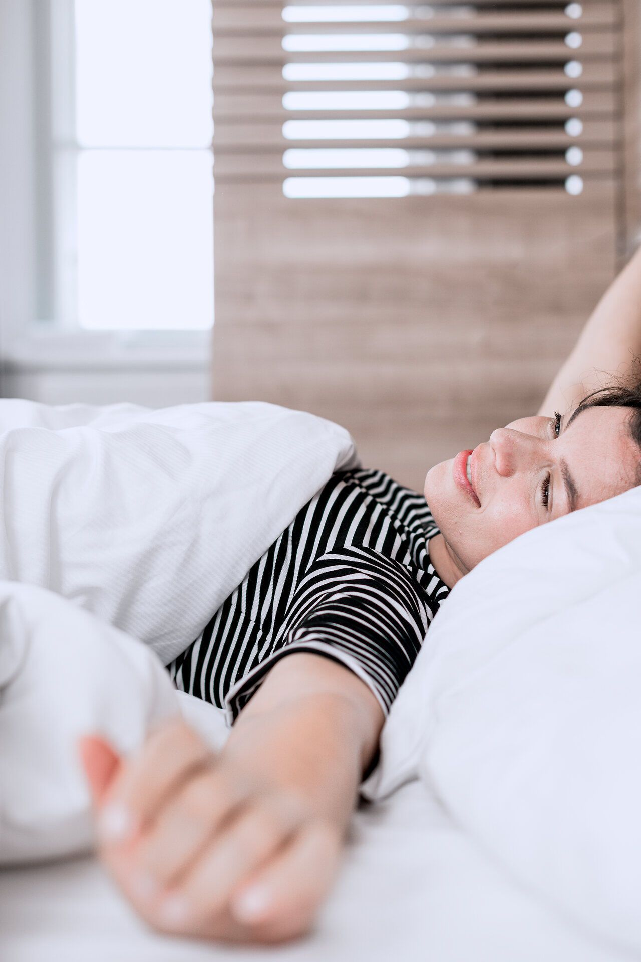 Frau liegt in einem Hotelbett und streckt sich nach dem Aufwachen.