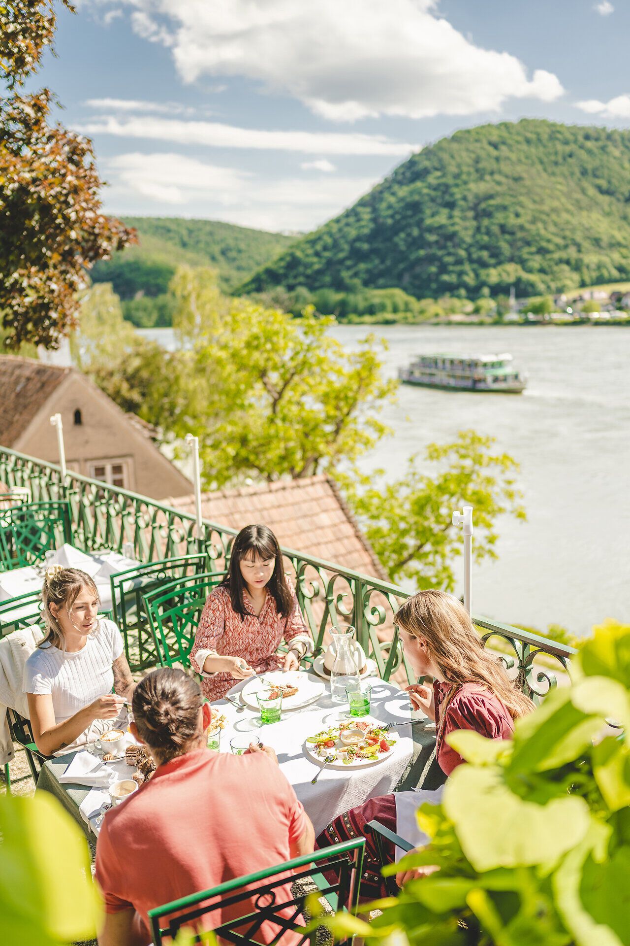 Drei Mädchen und ein Mann sitzen an einem gedeckten Tisch an der Donau.