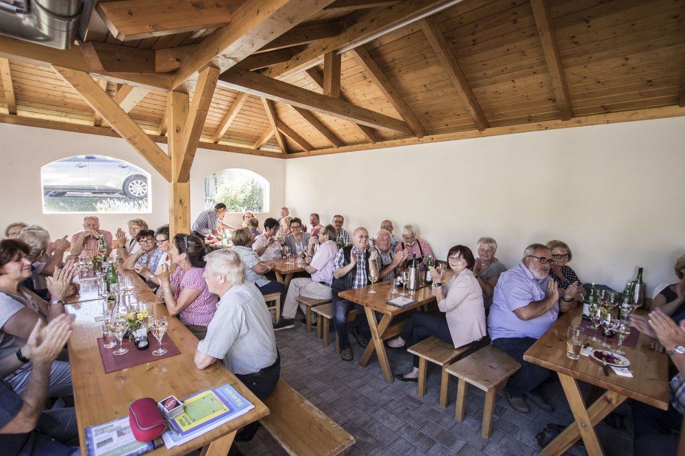 Menschen sitzen in einem Heurigenlokal an Holztischen und klatschen.