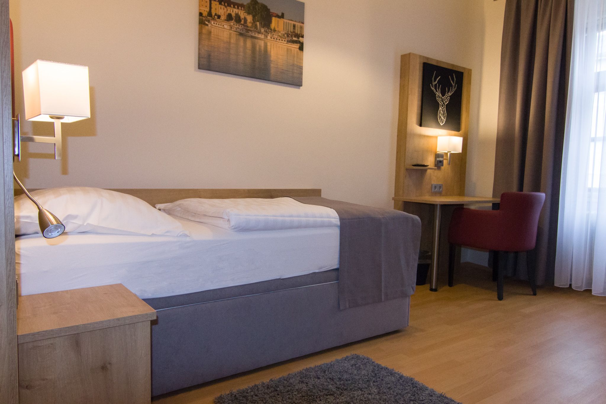 Einzelzimmer mit Bett, Schreibtisch und rotem Stuhl.